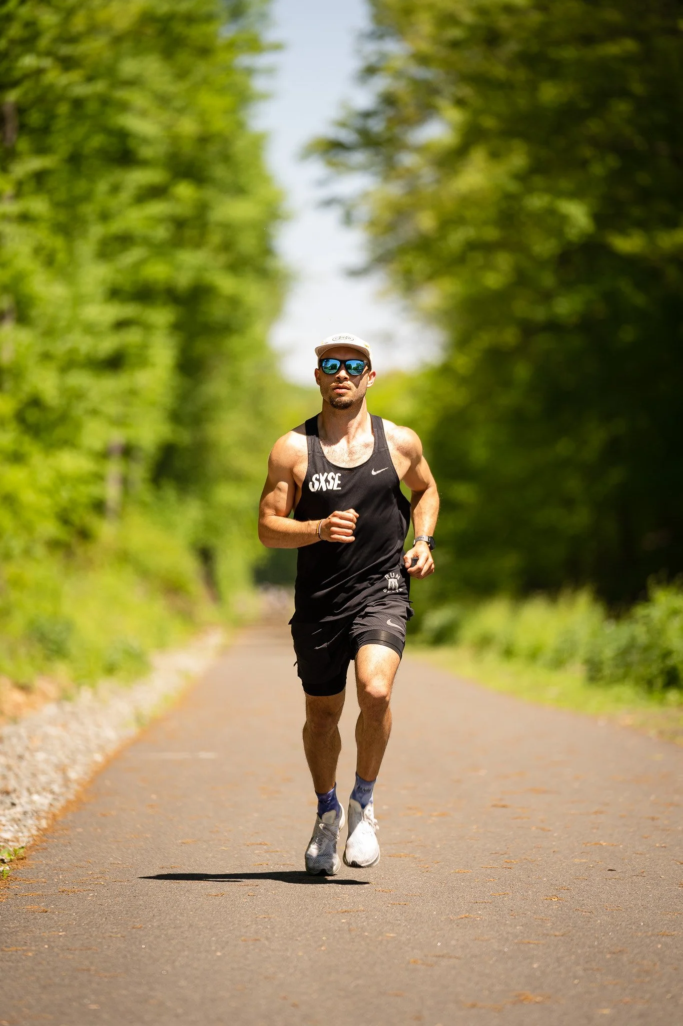 A man running on a paved path in a green, wooded area during daytime.
