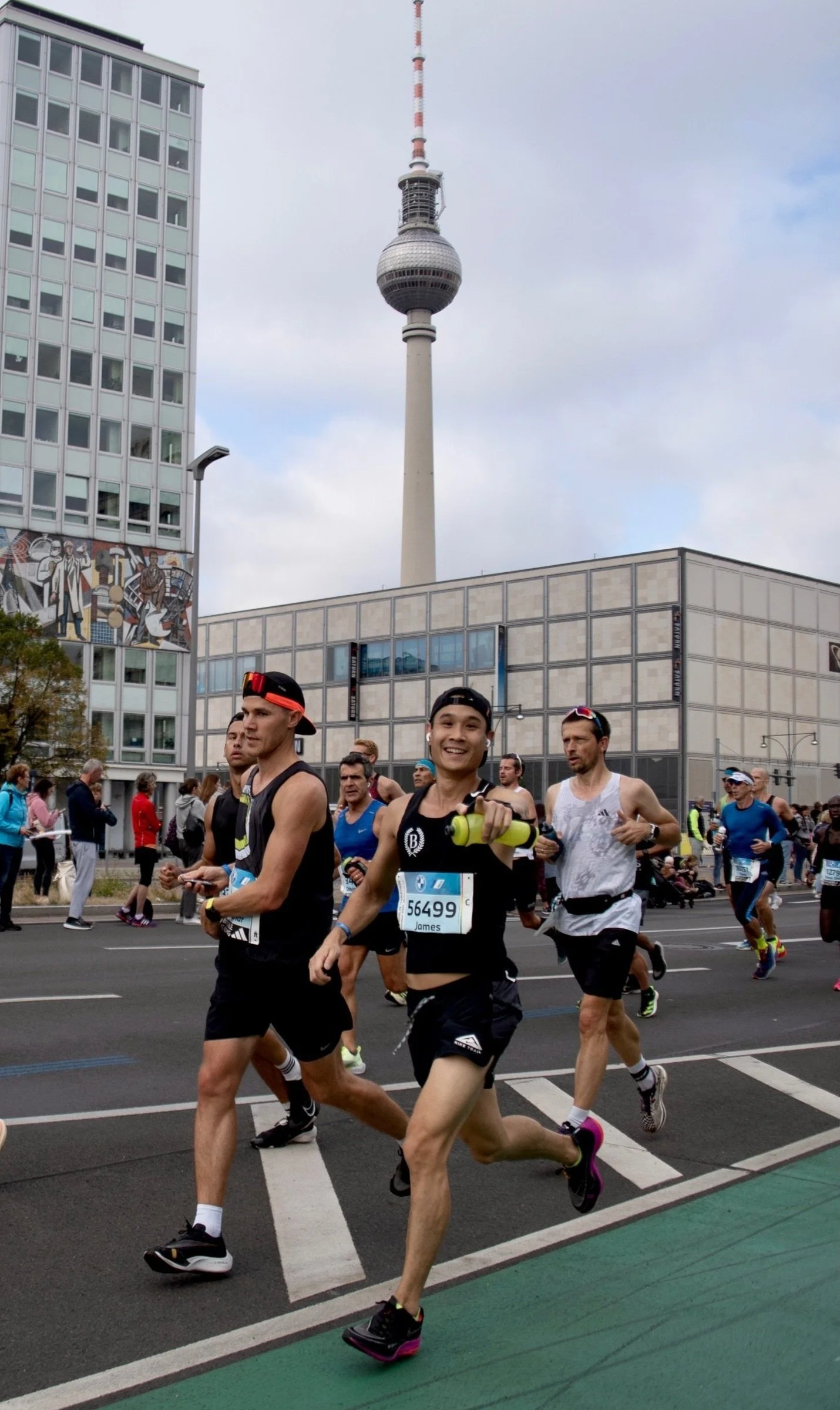 Marathon runners on a city street with the Berlin TV Tower in the background.