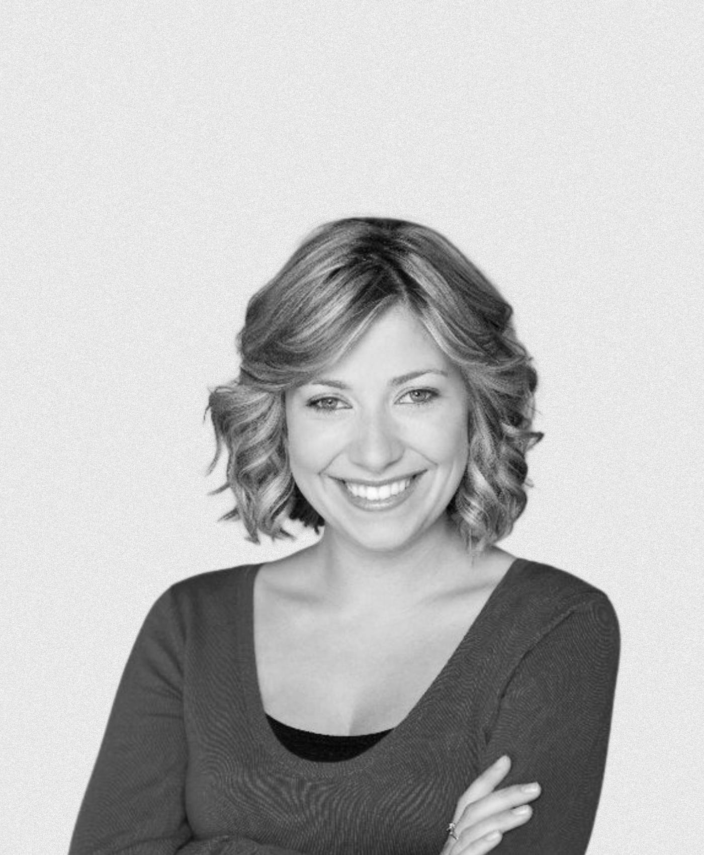 Black and white portrait of a woman with shoulder-length wavy hair, smiling, wearing a dark top with a wide neckline, standing against a plain background.