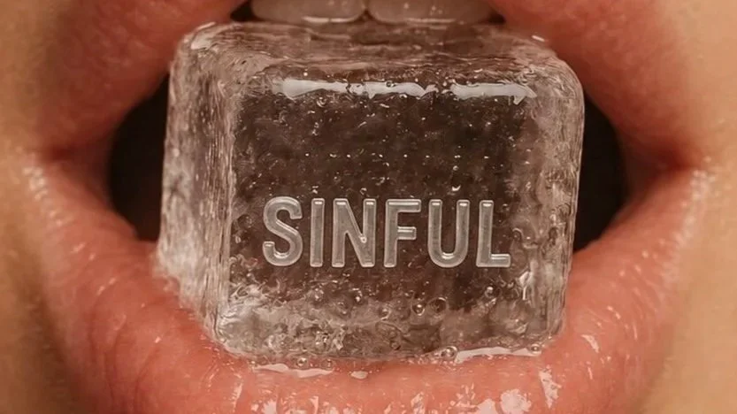 Close-up of lips holding a clear ice cube with the word "SINFUL" engraved on it.