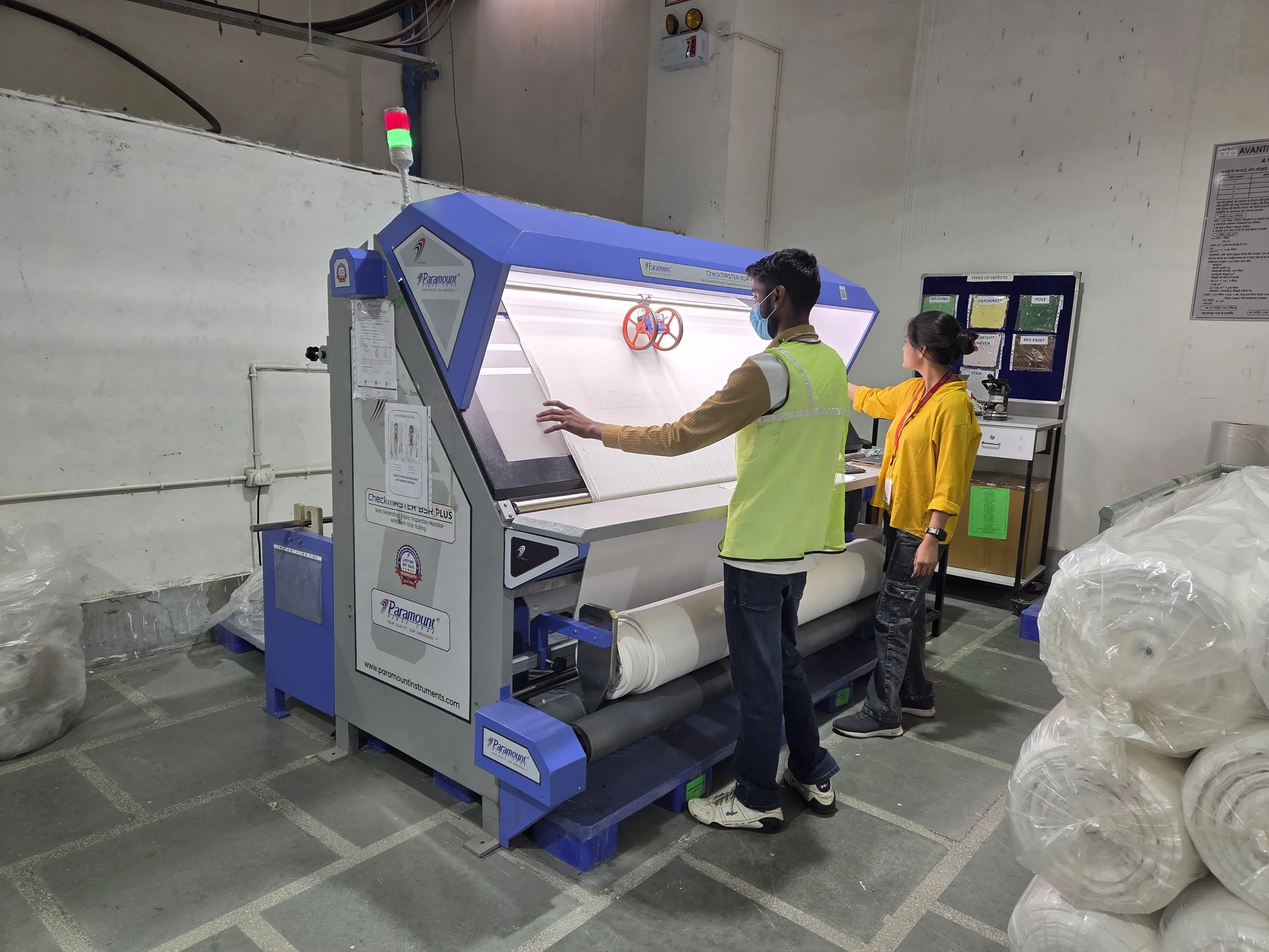 Two workers at a quality control station inspecting a rolled material on a conveyor in an industrial setting.