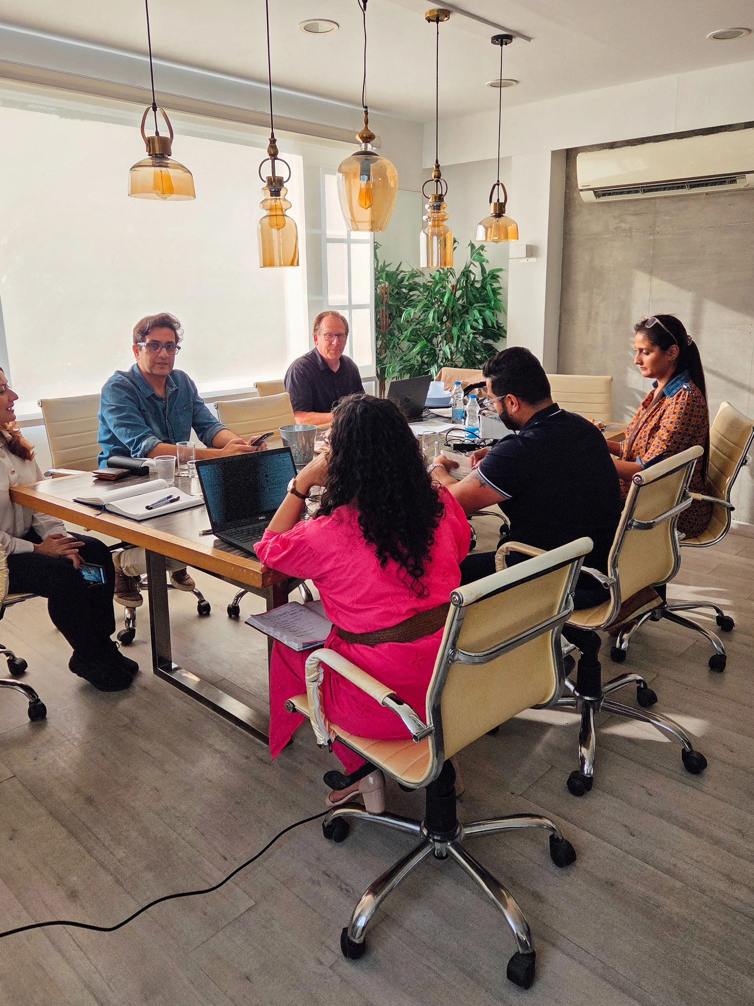 People sitting around a conference table in a meeting room, working on laptops and taking notes.