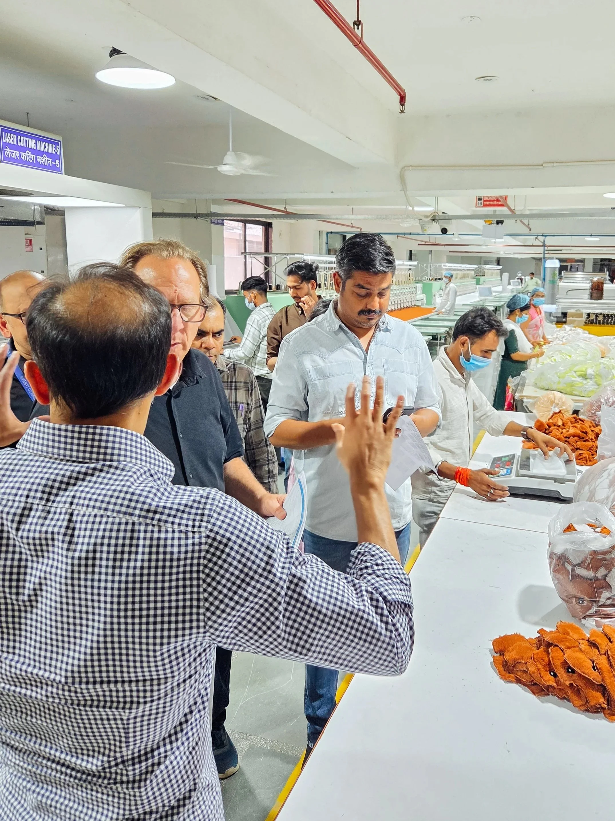 People in a factory or workshop inspecting and handling leather pieces, with some wearing masks, near workstations and equipment.