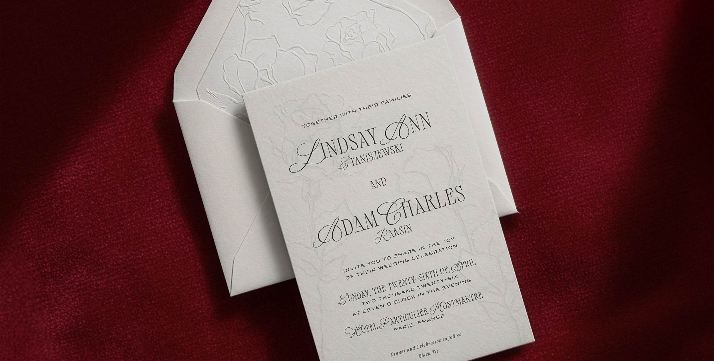 Letterpress printed wedding invitation with elegant black typography on a white background, placed on a red fabric surface, with an embossed floral pattern on the envelope lining.