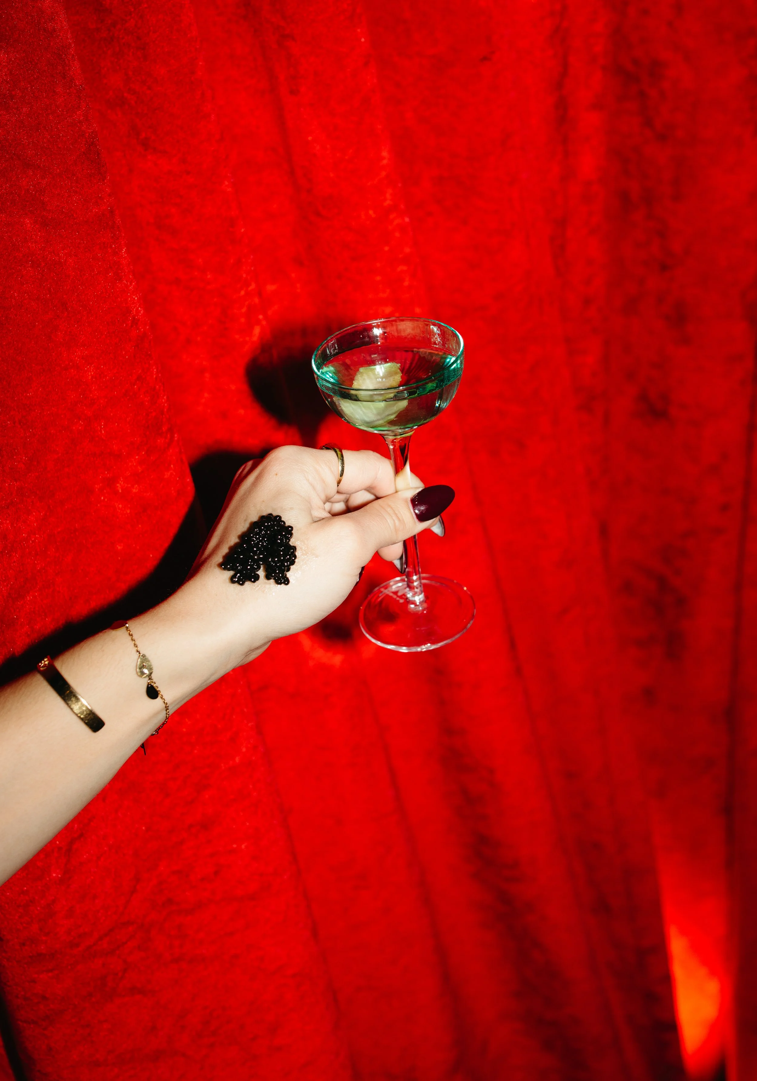 Hand holding a martini glass with a lime wedge against a red curtain background.