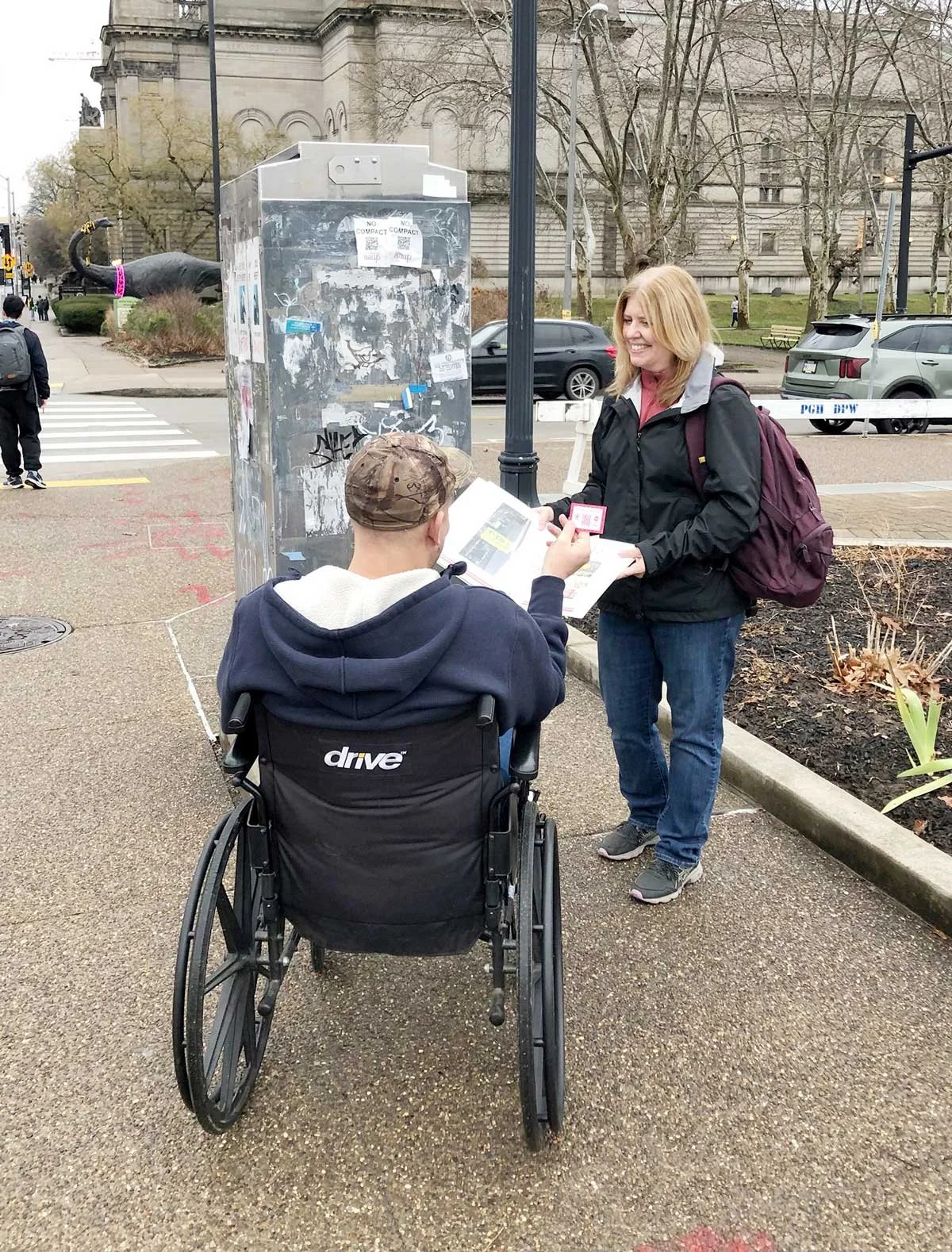 Artist Marsha Rollinger sitting on a bench outside in conversation with a man from one of the participating PittsBirds communities.