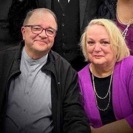 Two people, a man with glasses and a woman with blonde hair, sitting close together at a social gathering.