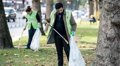 Two people cleaning up a park and using litter pickers with trash bags.