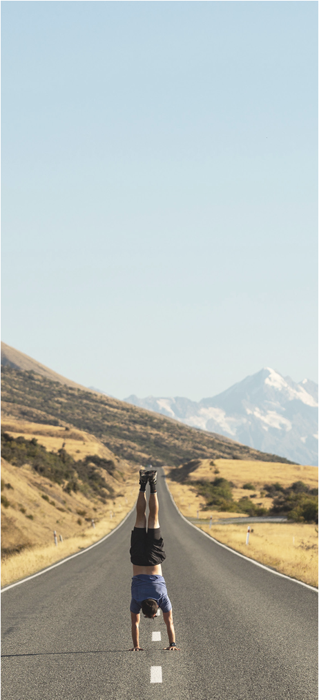 Person doing a handstand in the middle of a deserted road in a scenic mountainous area.