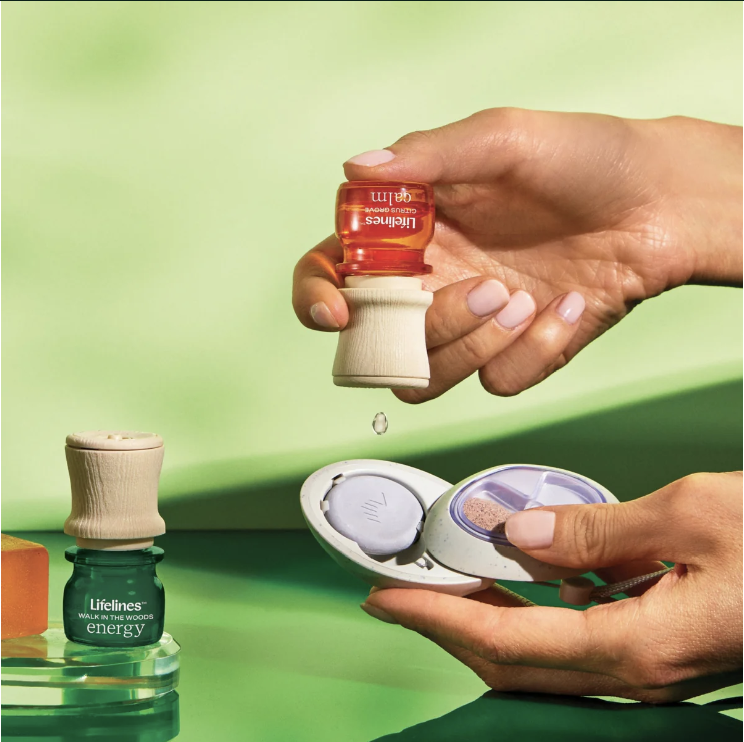 Person holding a small container of red tinted eye drops with a single drop falling, open contact lens case with a pink lens inside, and various vitamin bottles on a green background.