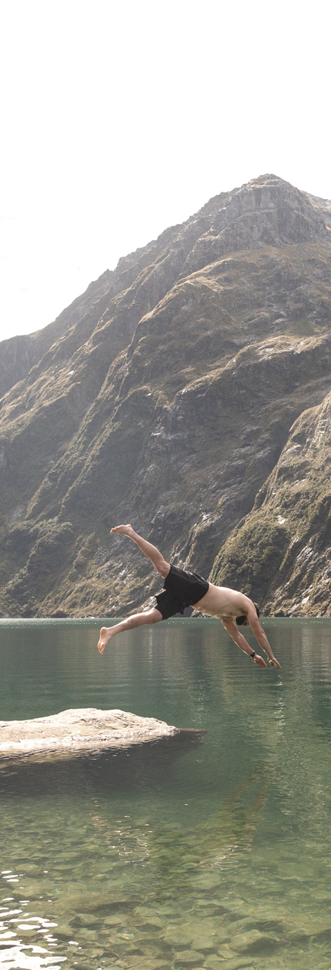 A man in black shorts diving into a lake with mountainous terrain in the background.