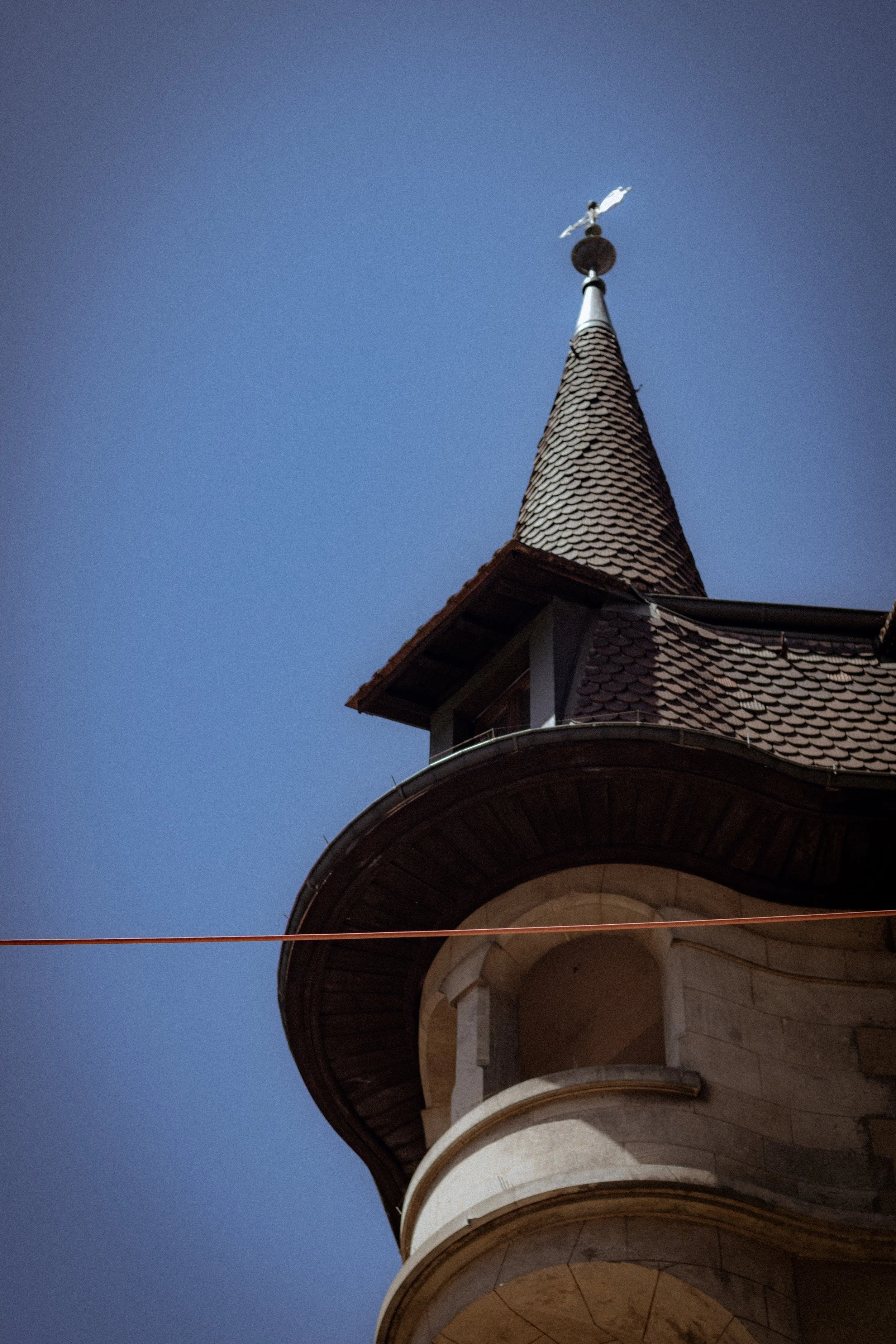 View of a church steeple with a weather vane on top against a clear blue sky.