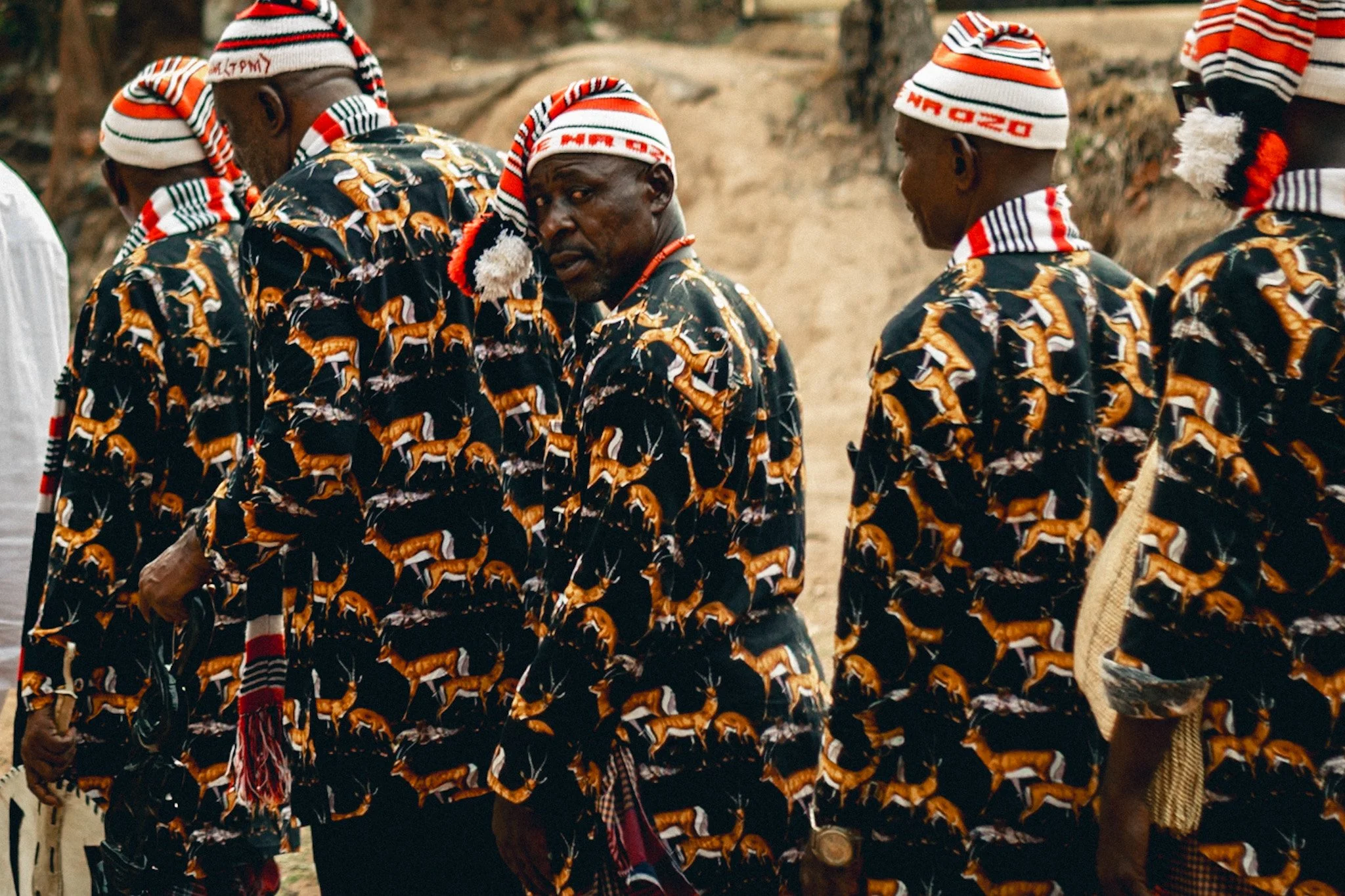 A group of men dressed in black clothing with a tiger print, wearing white knit caps with red and black stripes, standing outdoors and engaged in conversation.