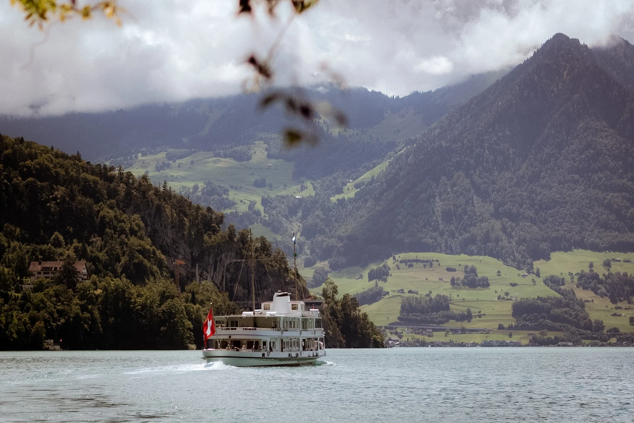 A white boat sailing on a lake with lush green mountains and cloudy sky in the background.