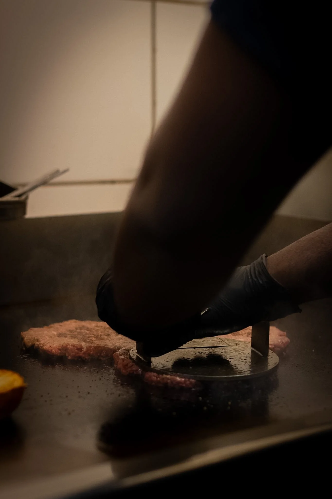 Person cooking ground meat on a stovetop with a round metal trivet, with a small piece of lemon or orange in the bottom left corner.