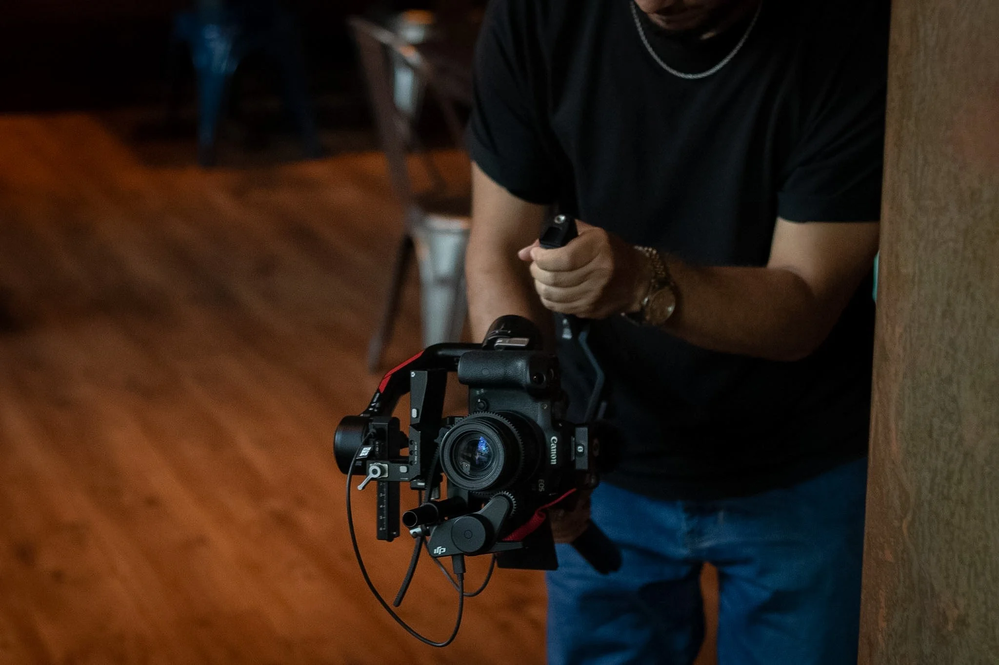 Person wearing black t-shirt adjusting camera on a tripod in indoor setting.