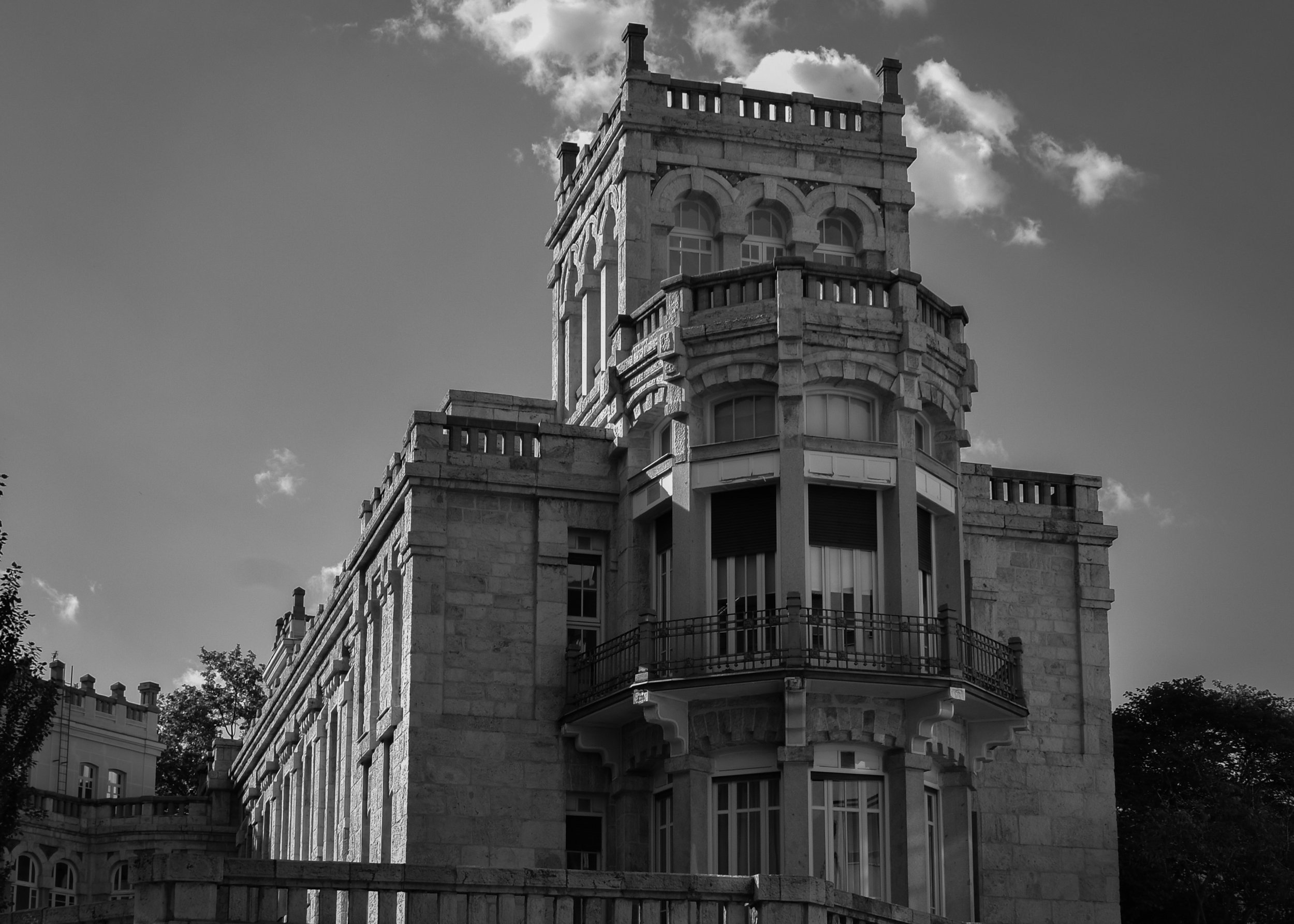 A historic stone building with a tower featuring arched windows and decorative balustrades, set against a partly cloudy sky.