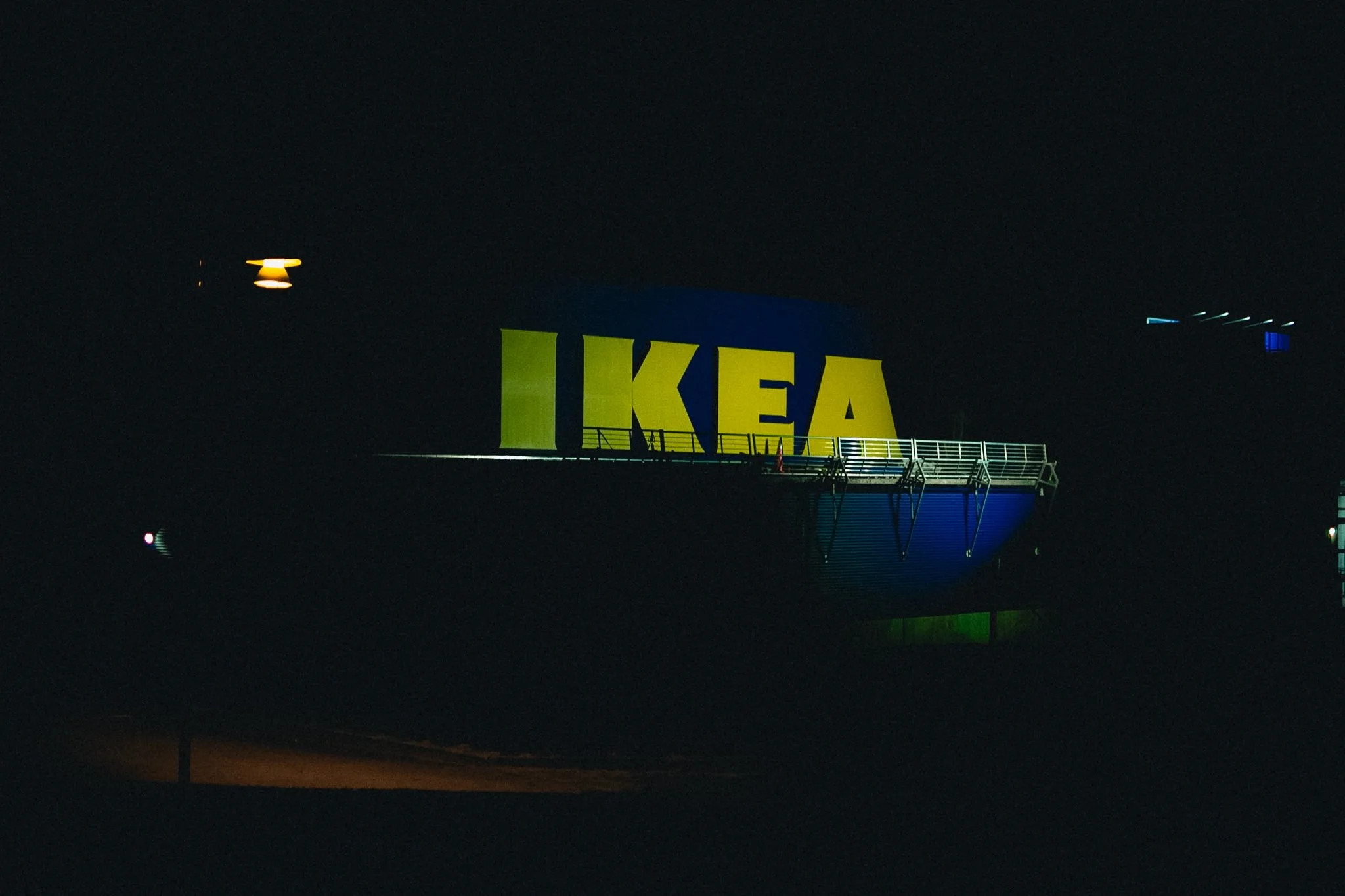Nighttime photo of an IKEA sign lit up against the dark sky, with a platform or balcony in front of it.