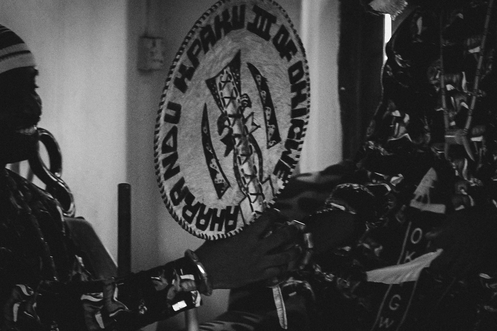 A black and white photo of a sign for the Washington Football Team with a Native American headdress logo in the center, hanging on a wall inside a room with motorcycle helmets on display.