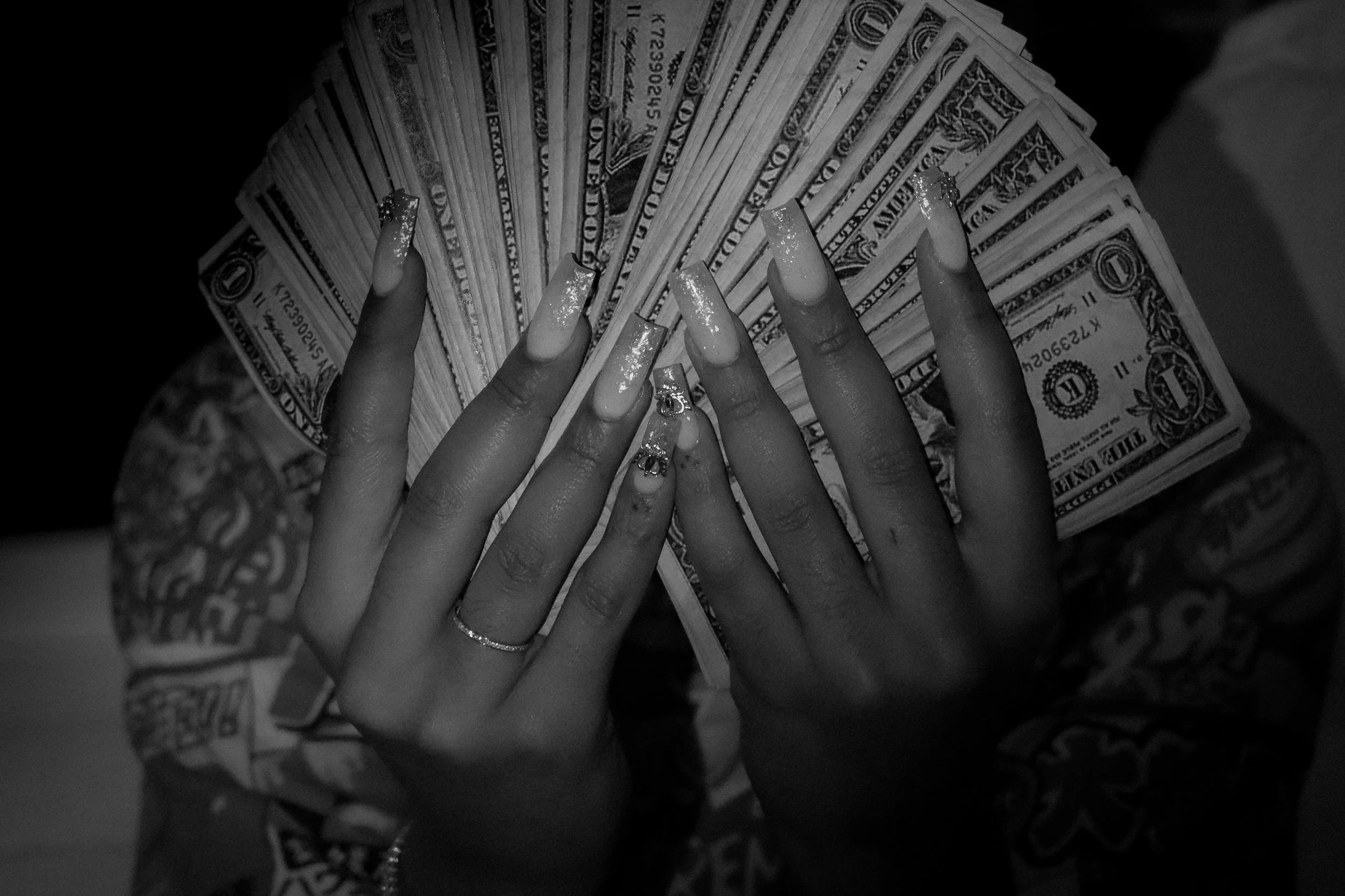 Black and white photo of hands with long, decorated acrylic nails holding a fan of U.S. dollar bills.
