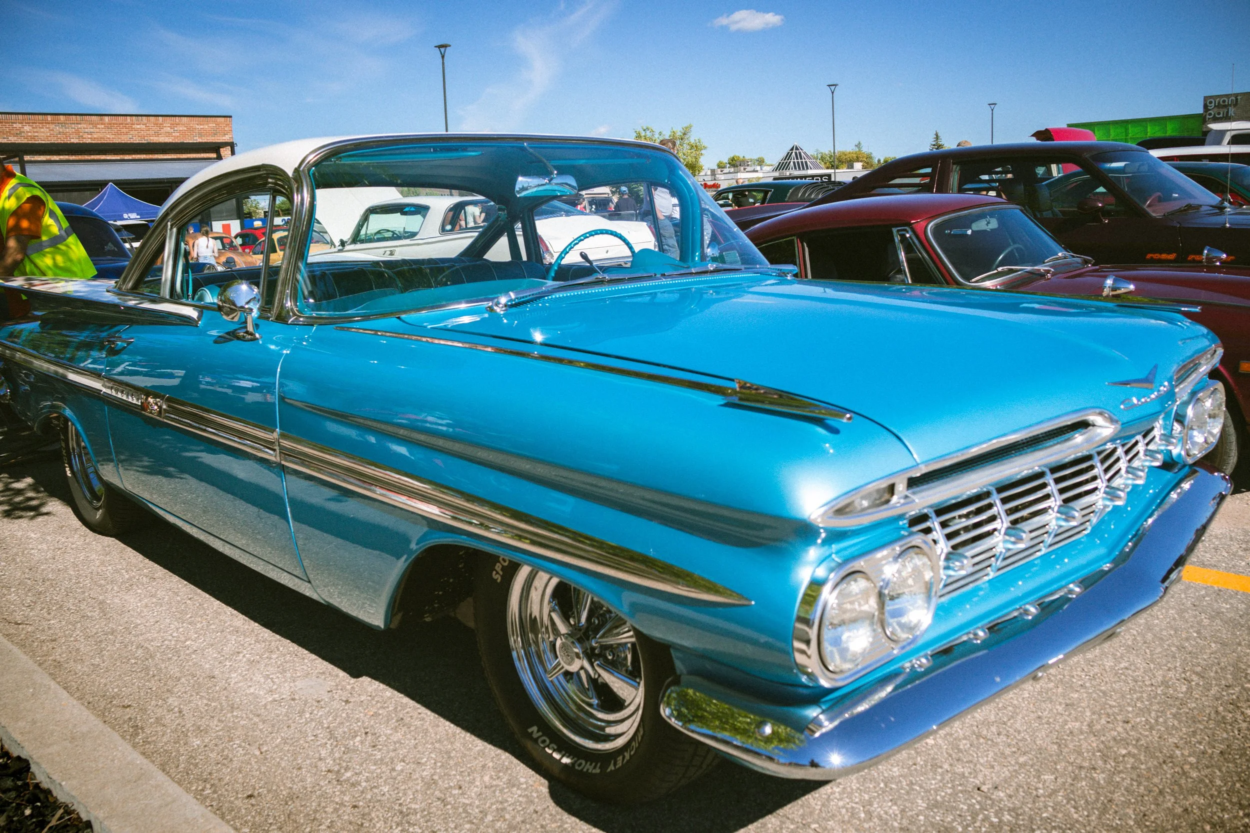 A vintage blue car with chrome detailing parked among other classic cars at a car show on a sunny day.
