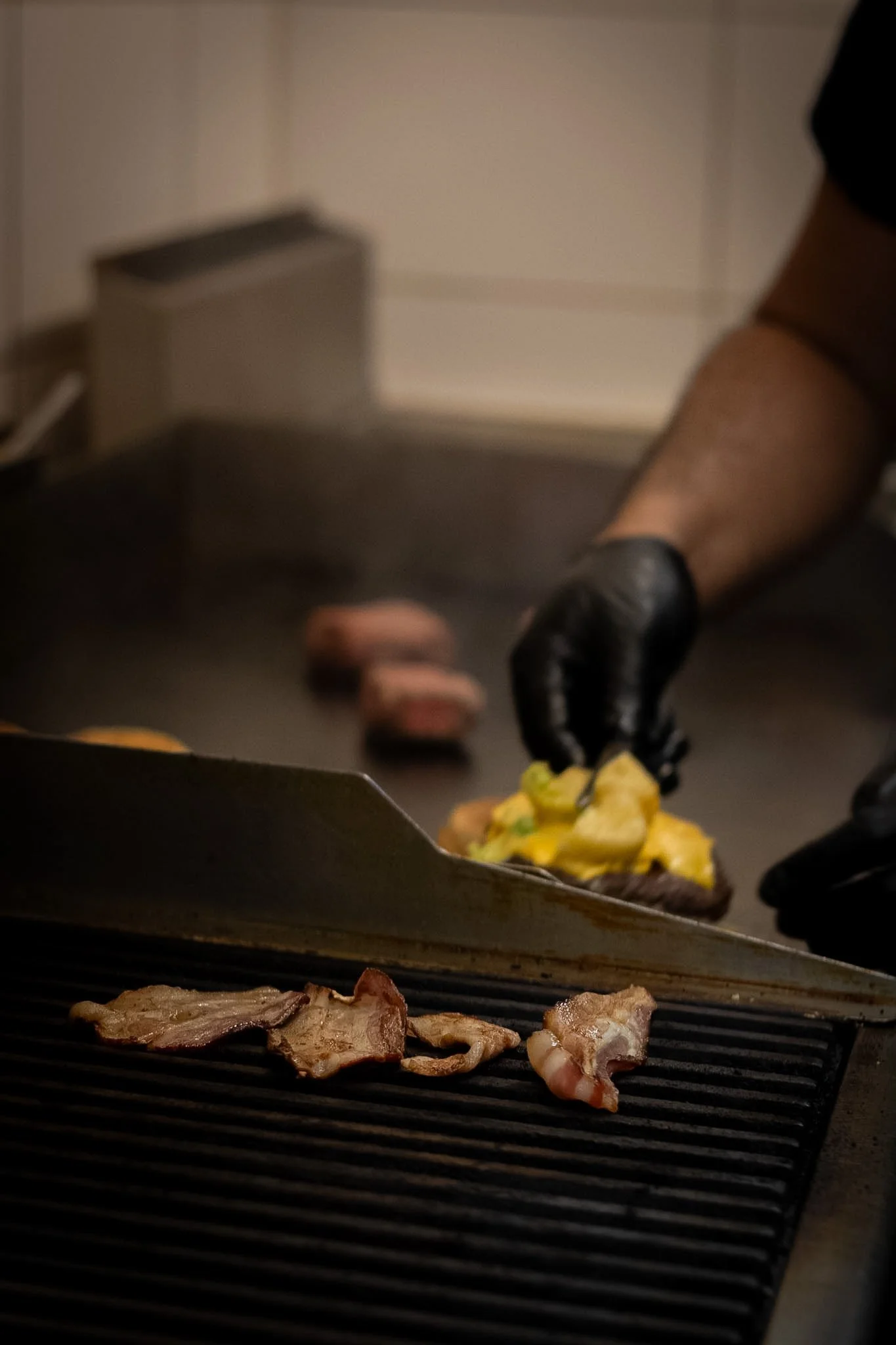 Person grilling bacon and scrambled eggs on a black grill pan, with a kitchen space in the background.