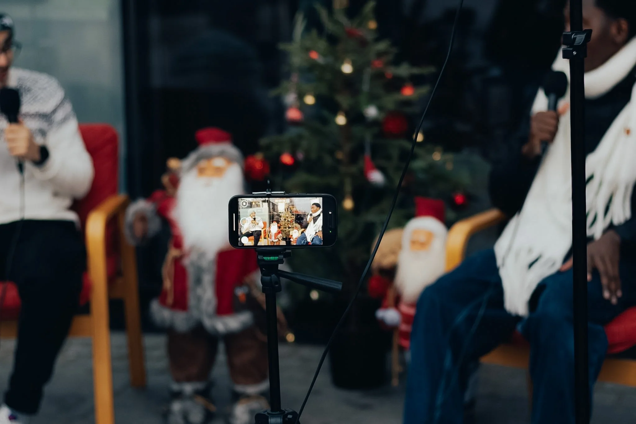 People recording a holiday event in front of a decorated Christmas tree.