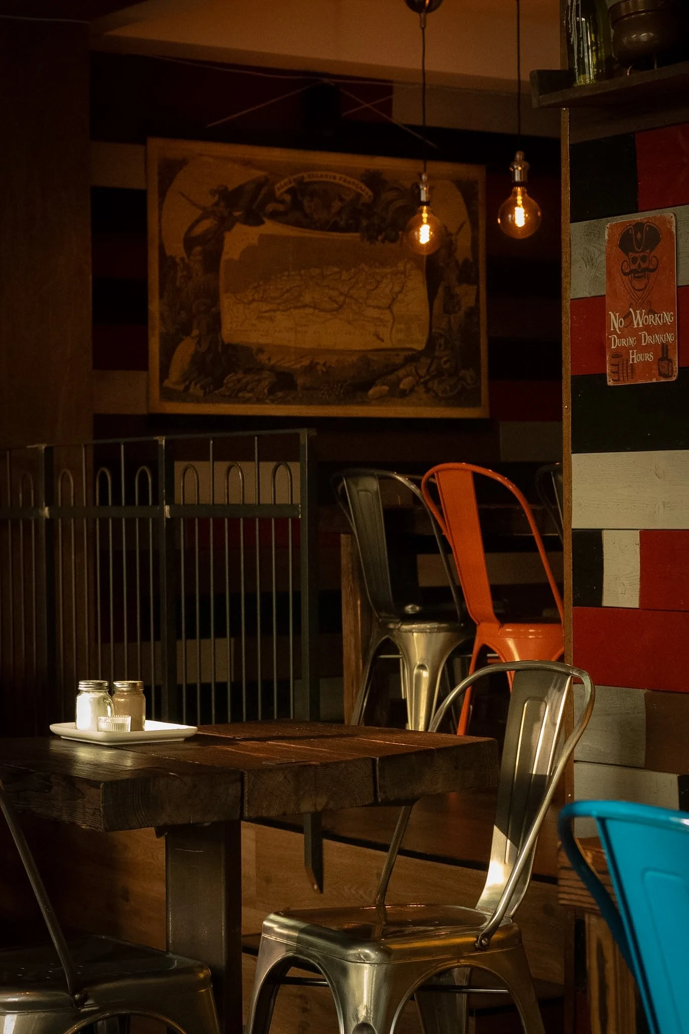 Part of a rustic restaurant interior with a wooden table, metal chairs, a wall decor with vintage sign, and ambient lighting.