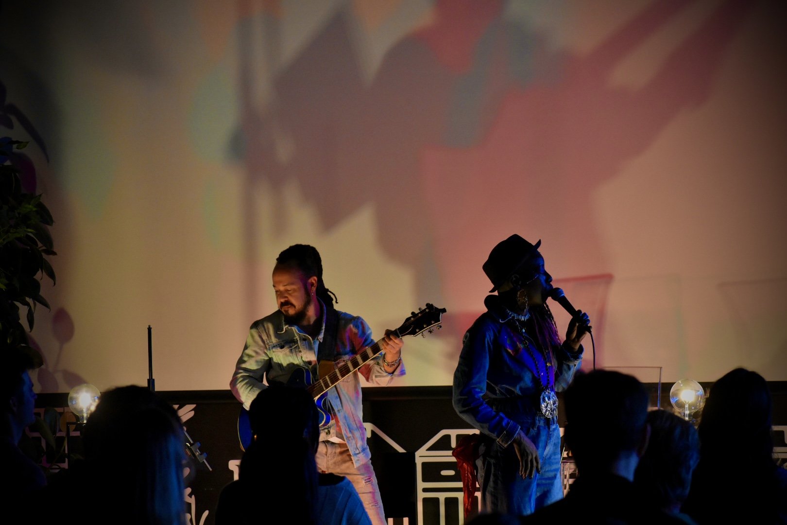 Musicians performing on stage with colorful lighting and audience members in the foreground.