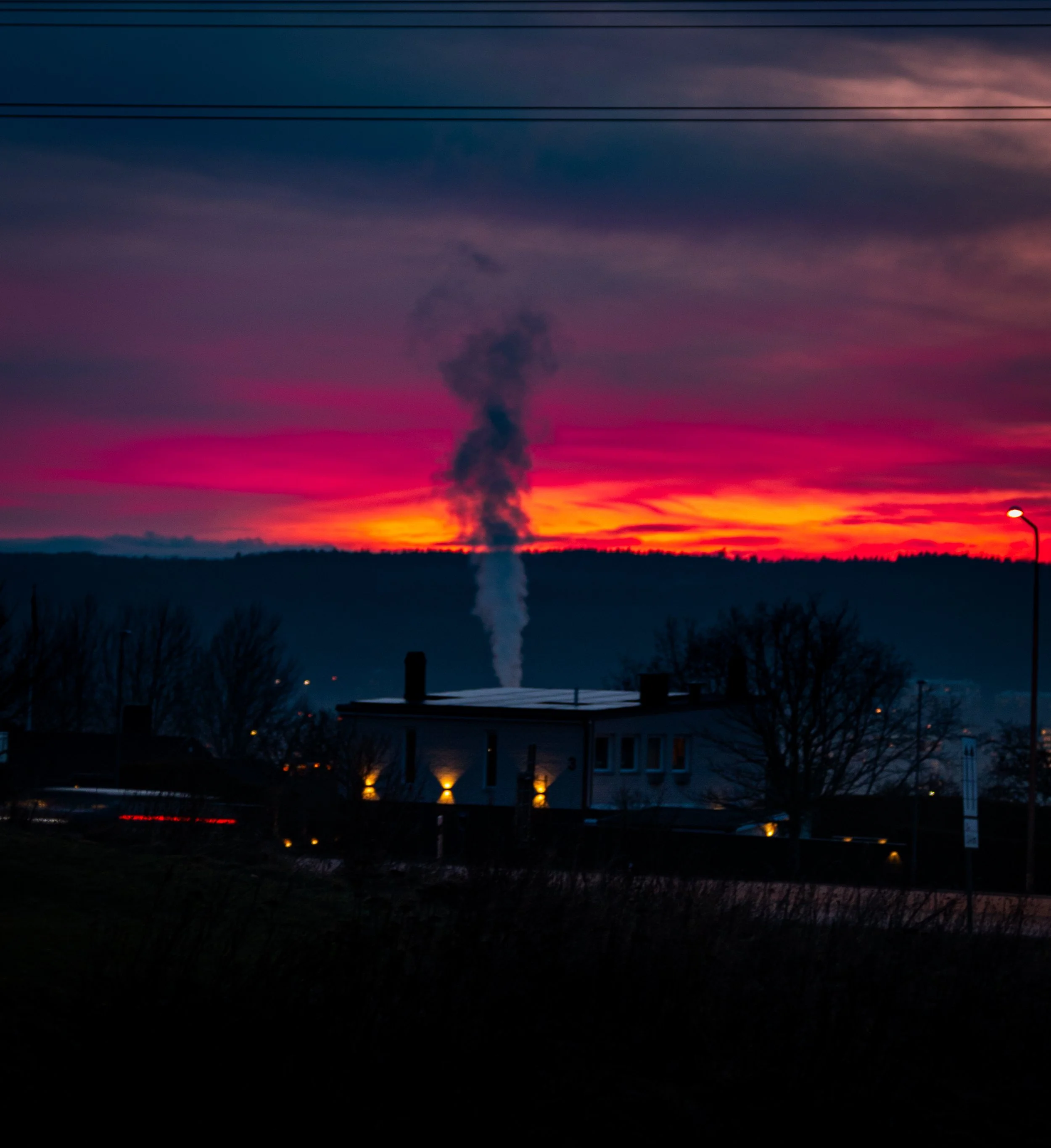 Colorful sunset sky with shades of pink, purple, and orange, and a dark plume of smoke rising from the horizon.