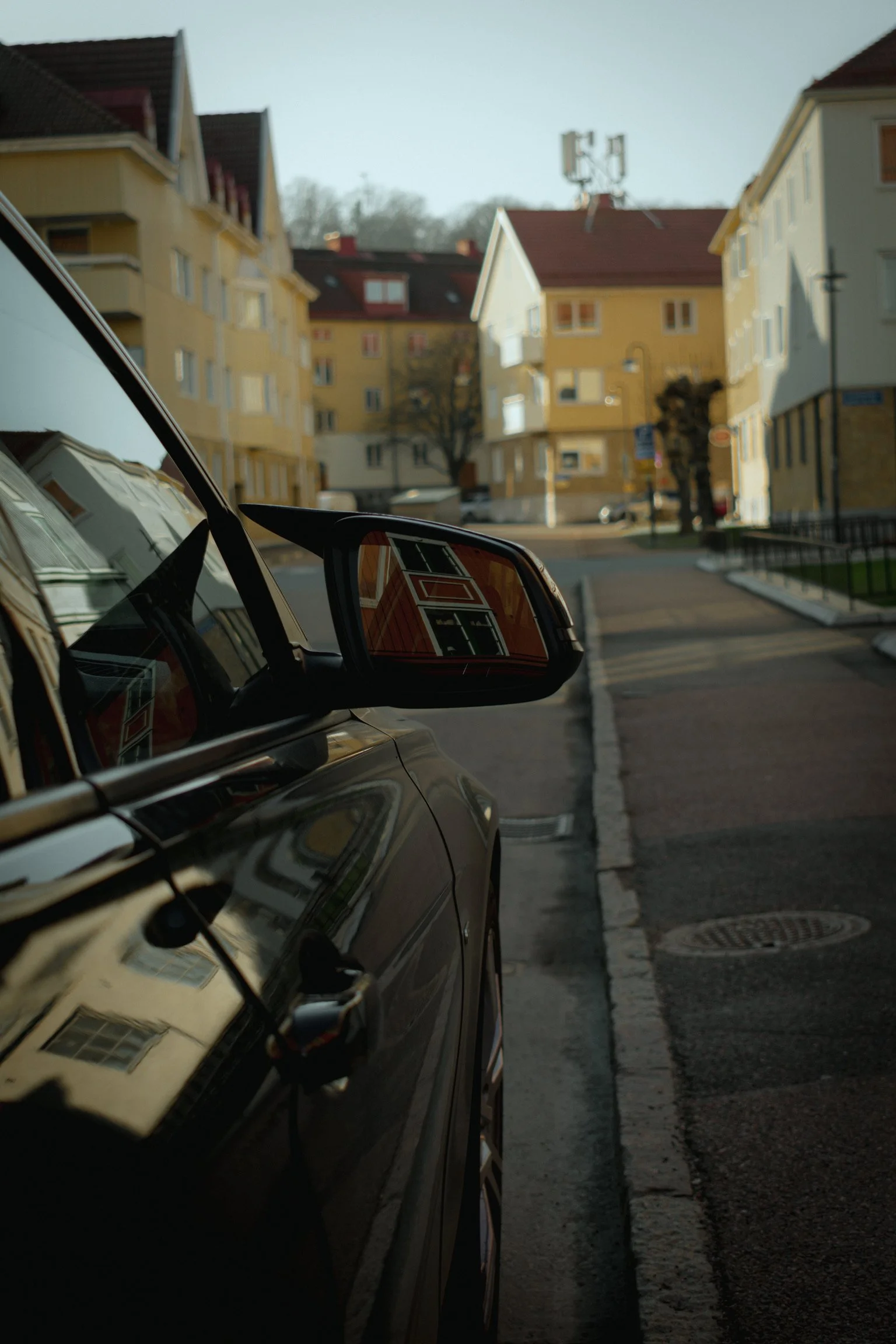 Side view of a parked car on a quiet residential street with yellow apartment buildings and a cell tower in the background.