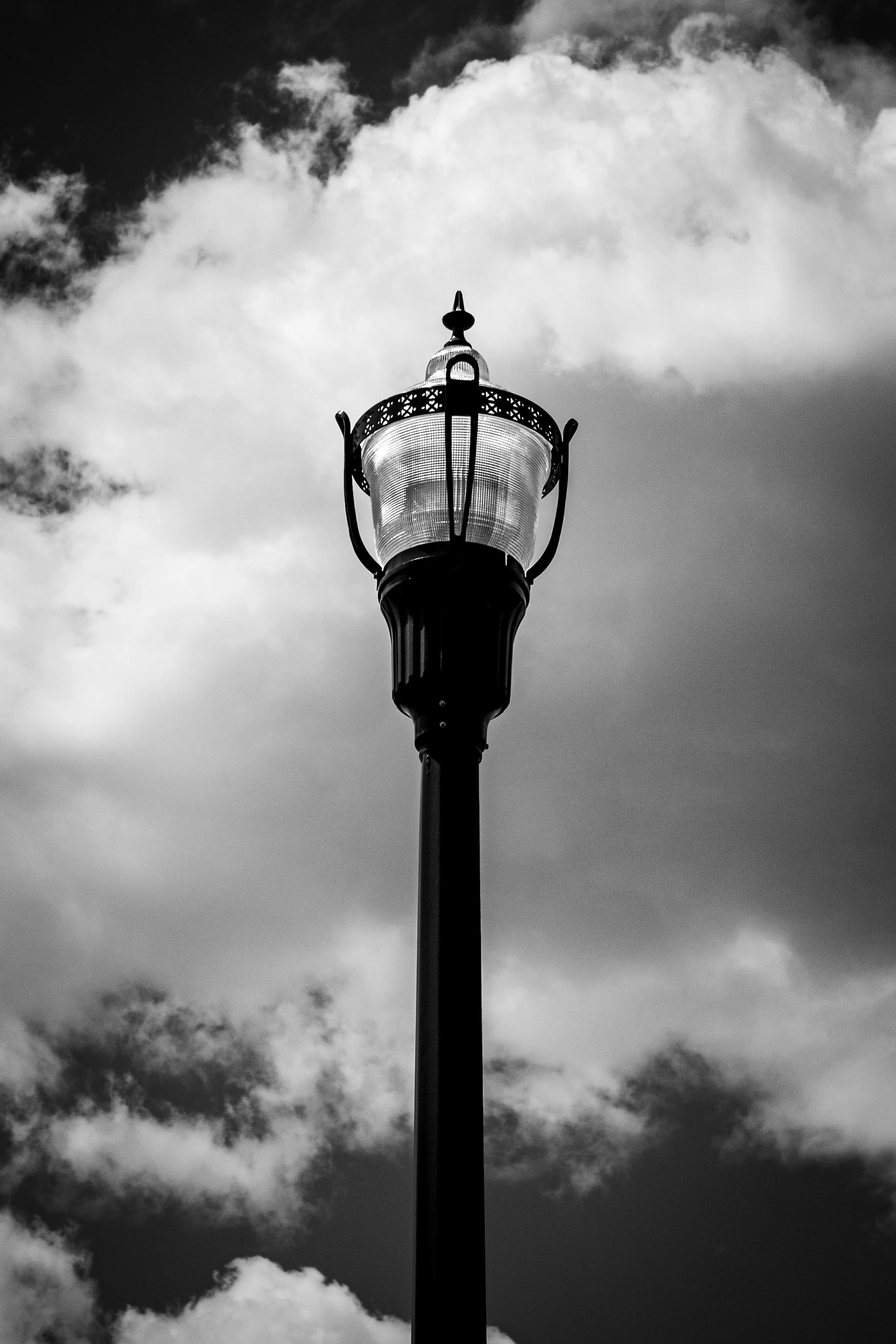 Black and white photograph of a vintage street lamp with a cloudy sky in the background.