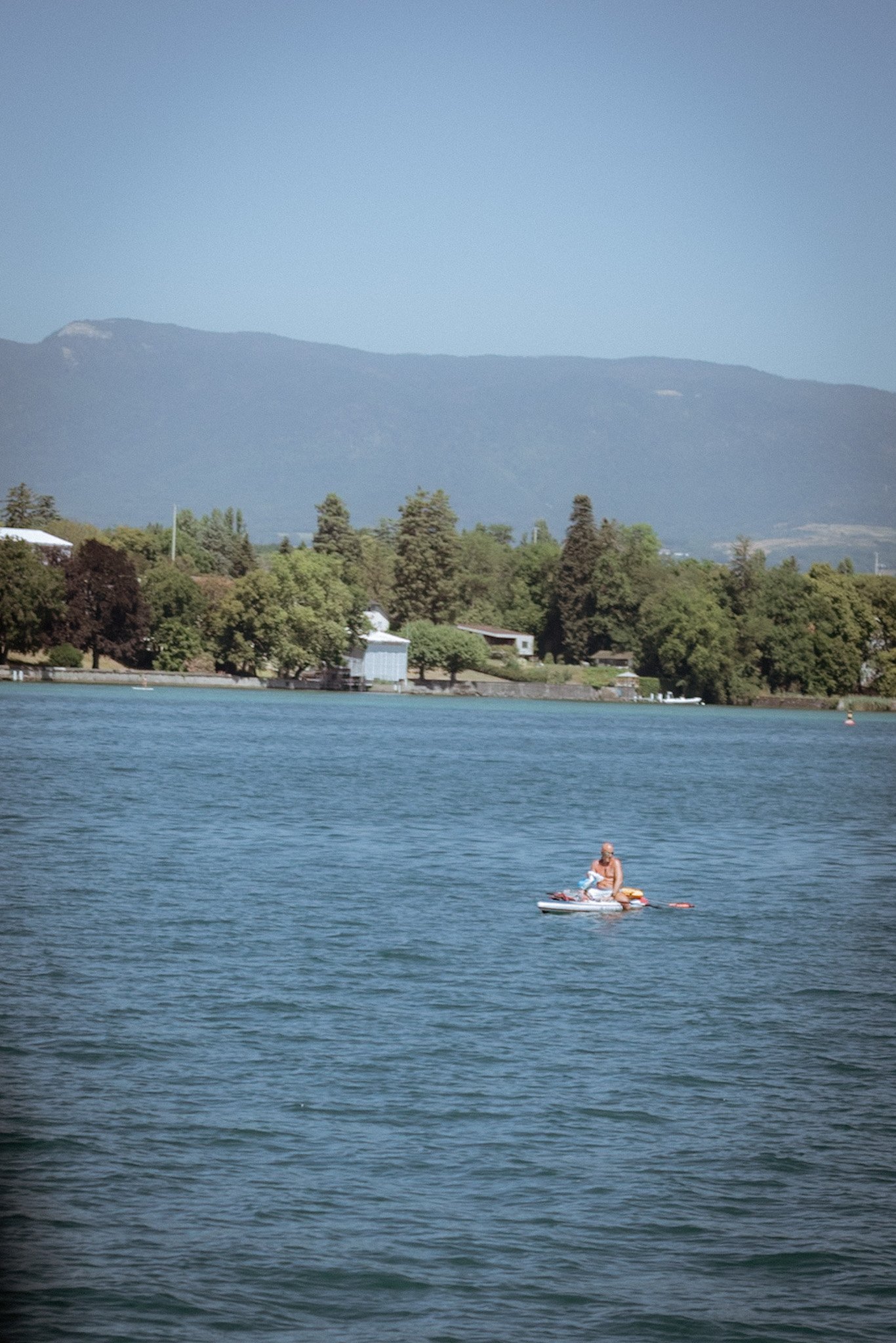 A person on a paddleboard on a lake with trees and mountains in the background.