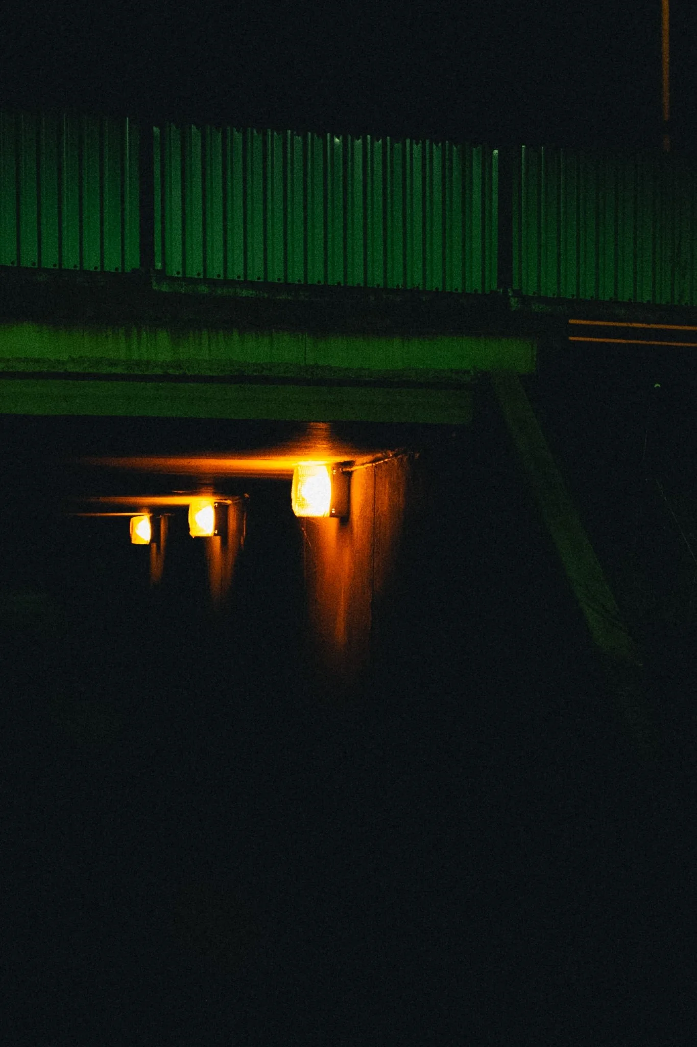 Night scene of a building with green illuminated walls and warm yellow lights reflected on water below.