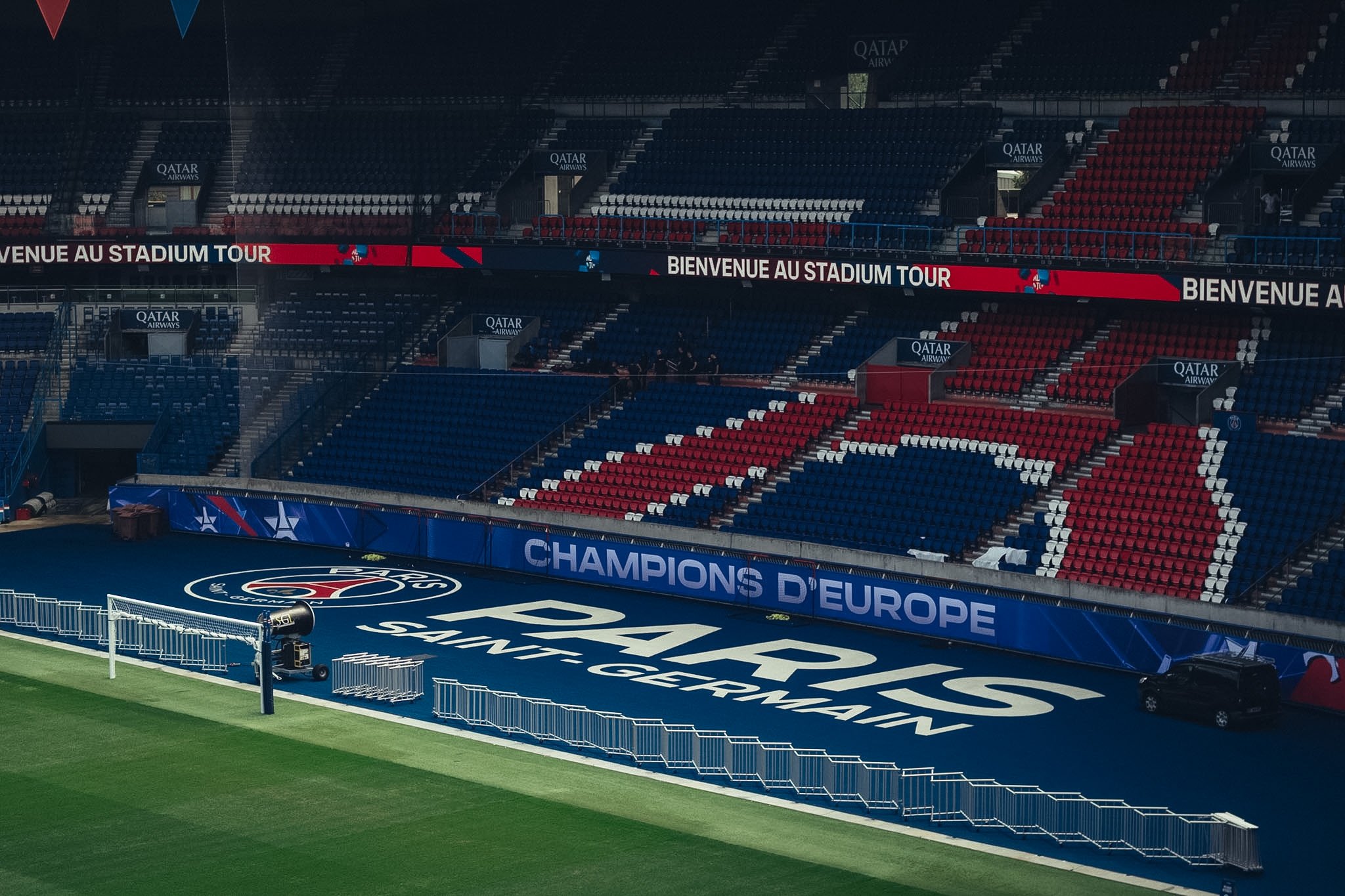 Empty football stadium with seating sections in red, white, and blue, and a field with UEFA Champions League branding and a goal on the side.