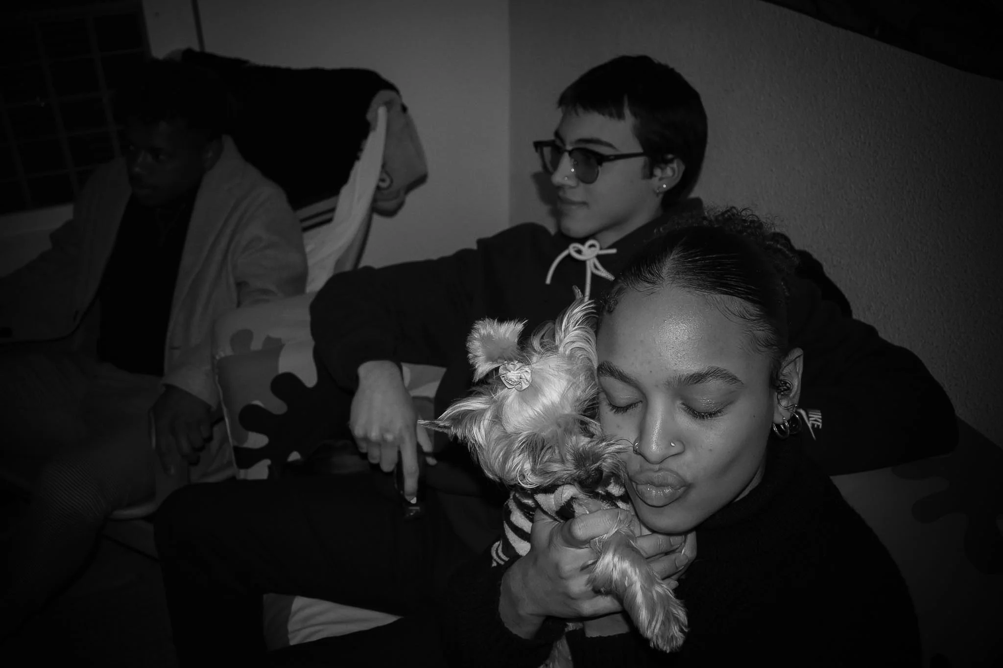 A group of people sitting closely, with one person holding a dog, all with their eyes closed and appearing relaxed or content.