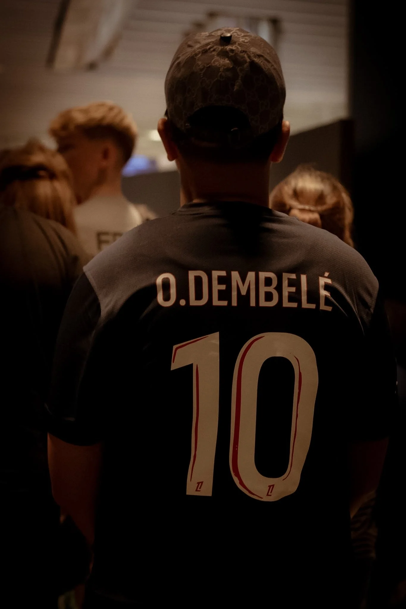 Back of a person wearing a sports jersey with the name O. Dembélé and the number 10, with a camouflage-patterned baseball cap.