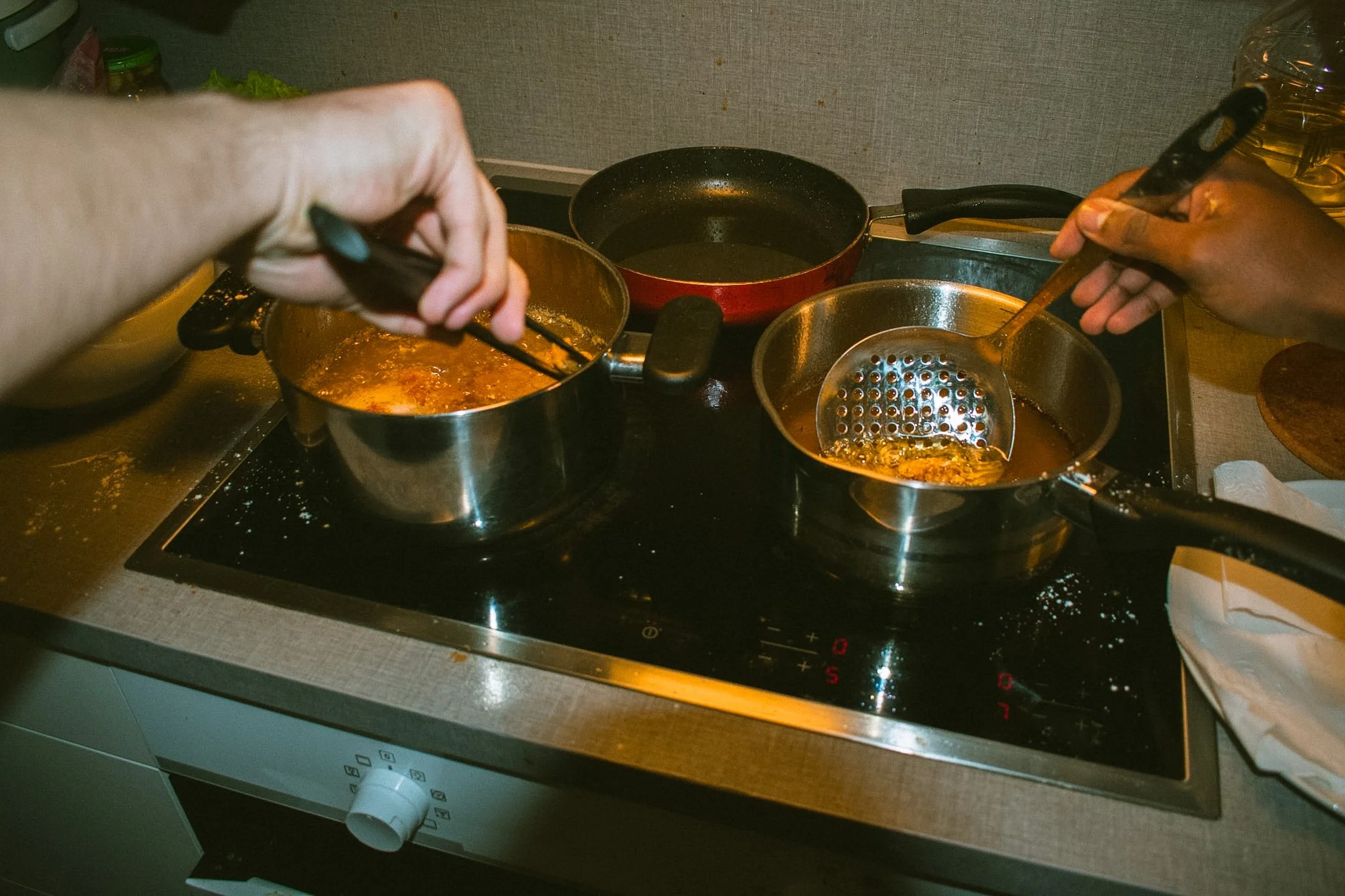 Hands cooking on stove with pots containing food, one pot steaming, in a kitchen.