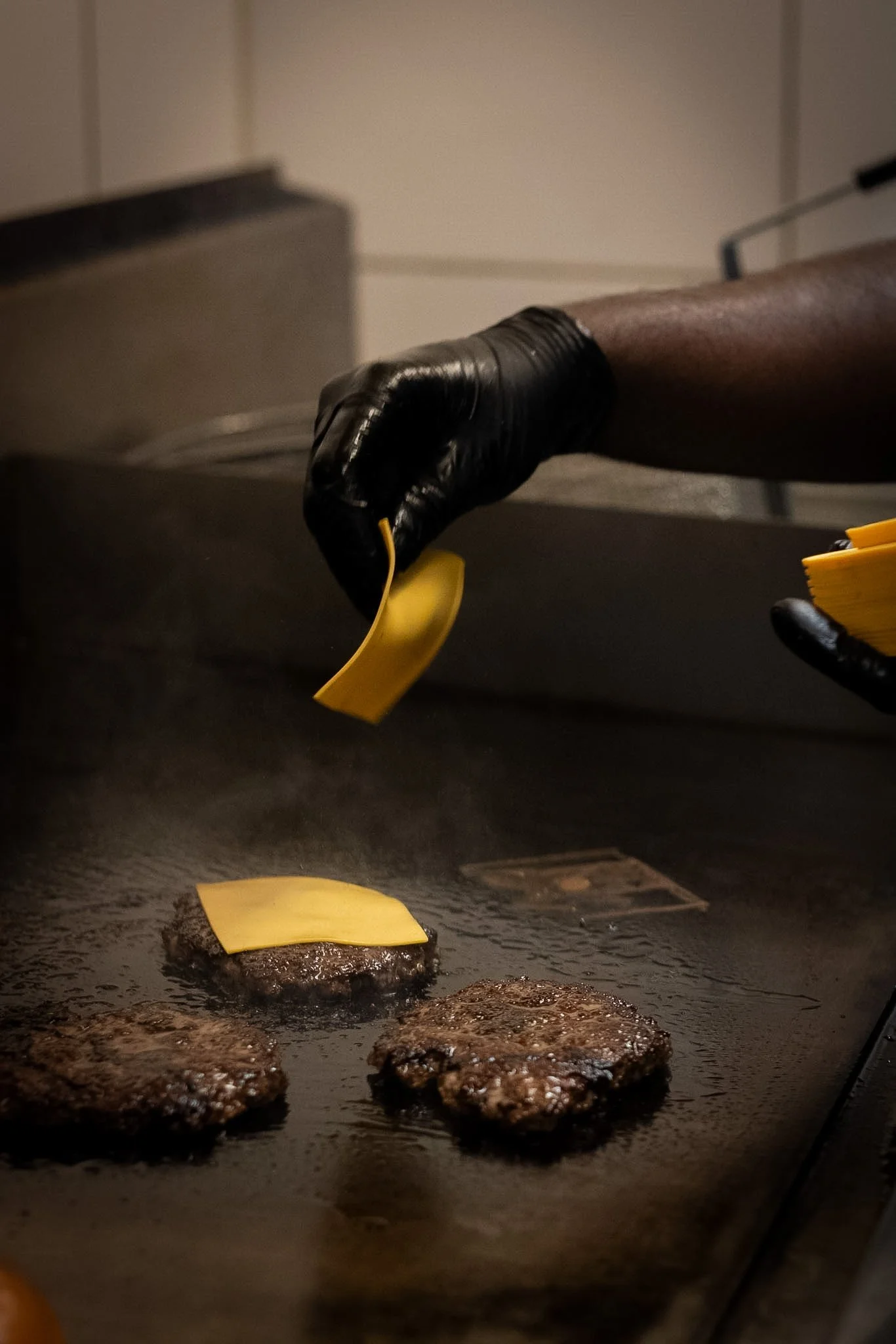 Cooking burgers on a flat-top griddle with slices of cheese placed on top.
