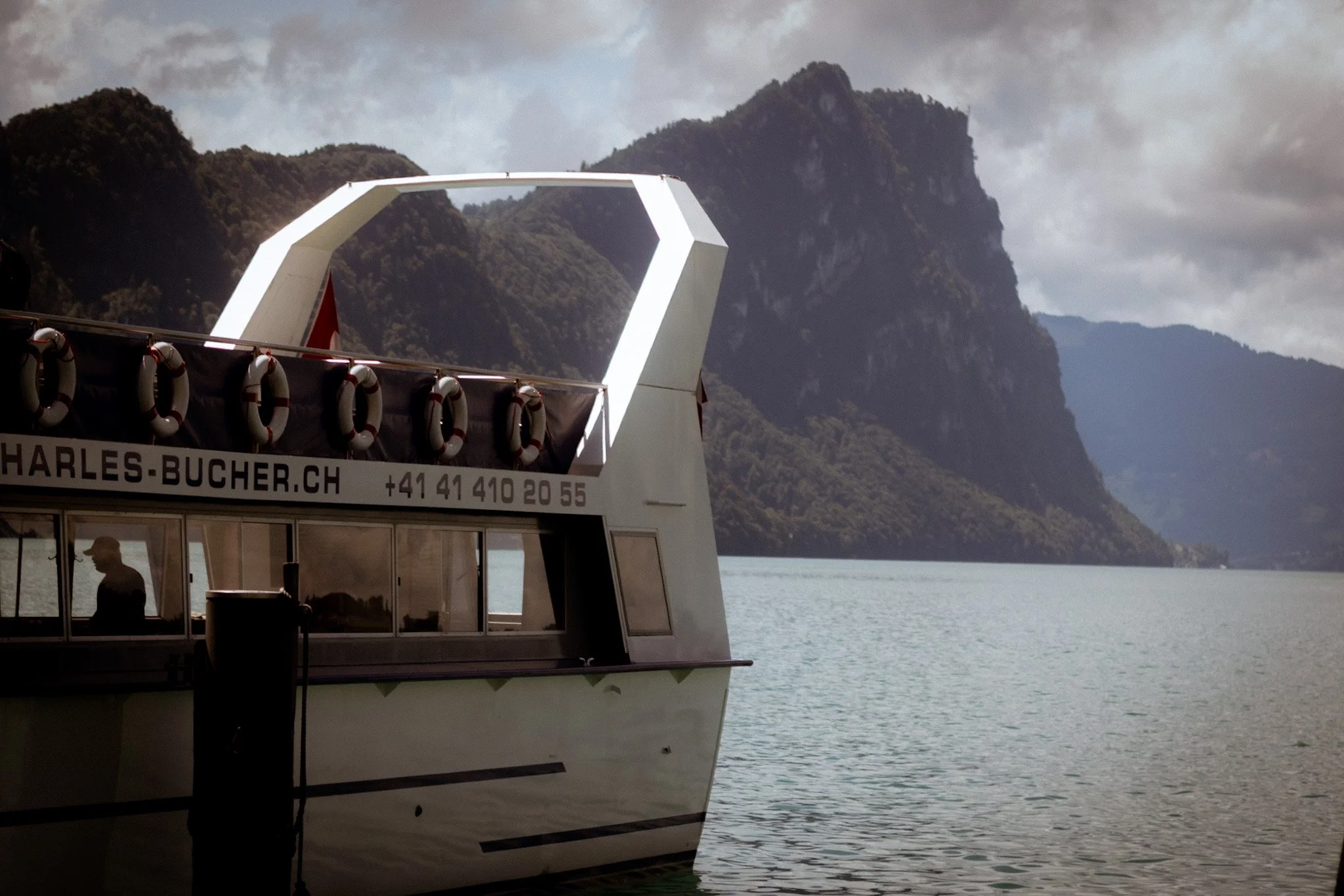 A large boat with a white structure on water with mountains in the background.