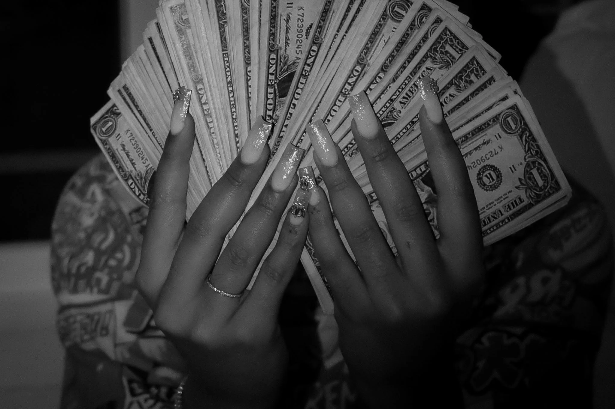 A person holding a fan of one-dollar bills, with long acrylic nails and rings on fingers.