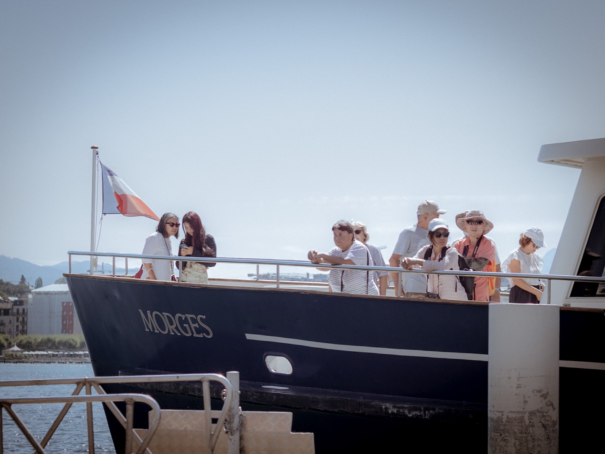 People gathered on a yacht named MORGES, with a French flag visible, under a clear sky with mountains in the background.
