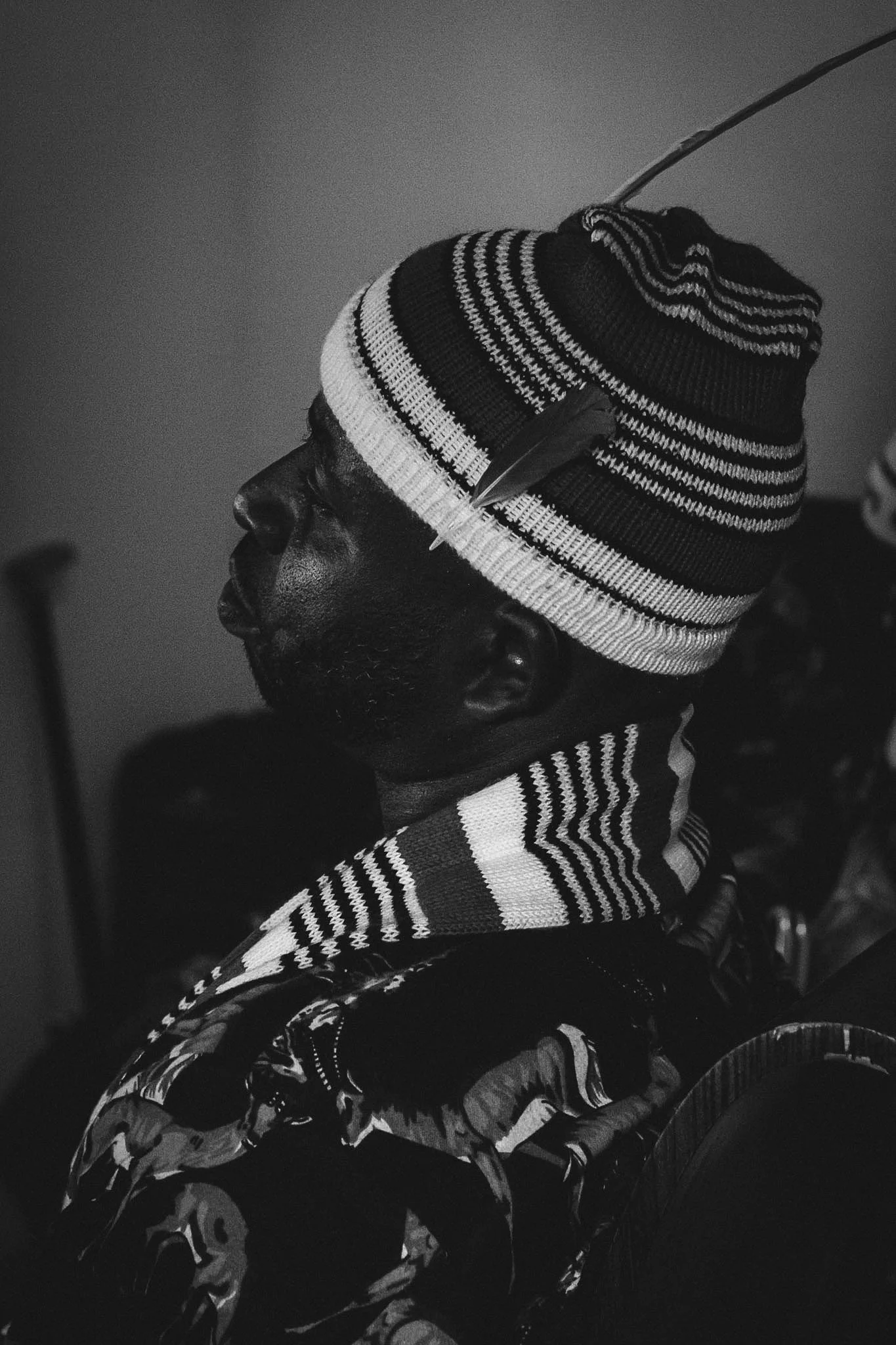 Black and white photo of a man in profile wearing a striped knit cap and patterned jacket, sitting in a wheelchair.
