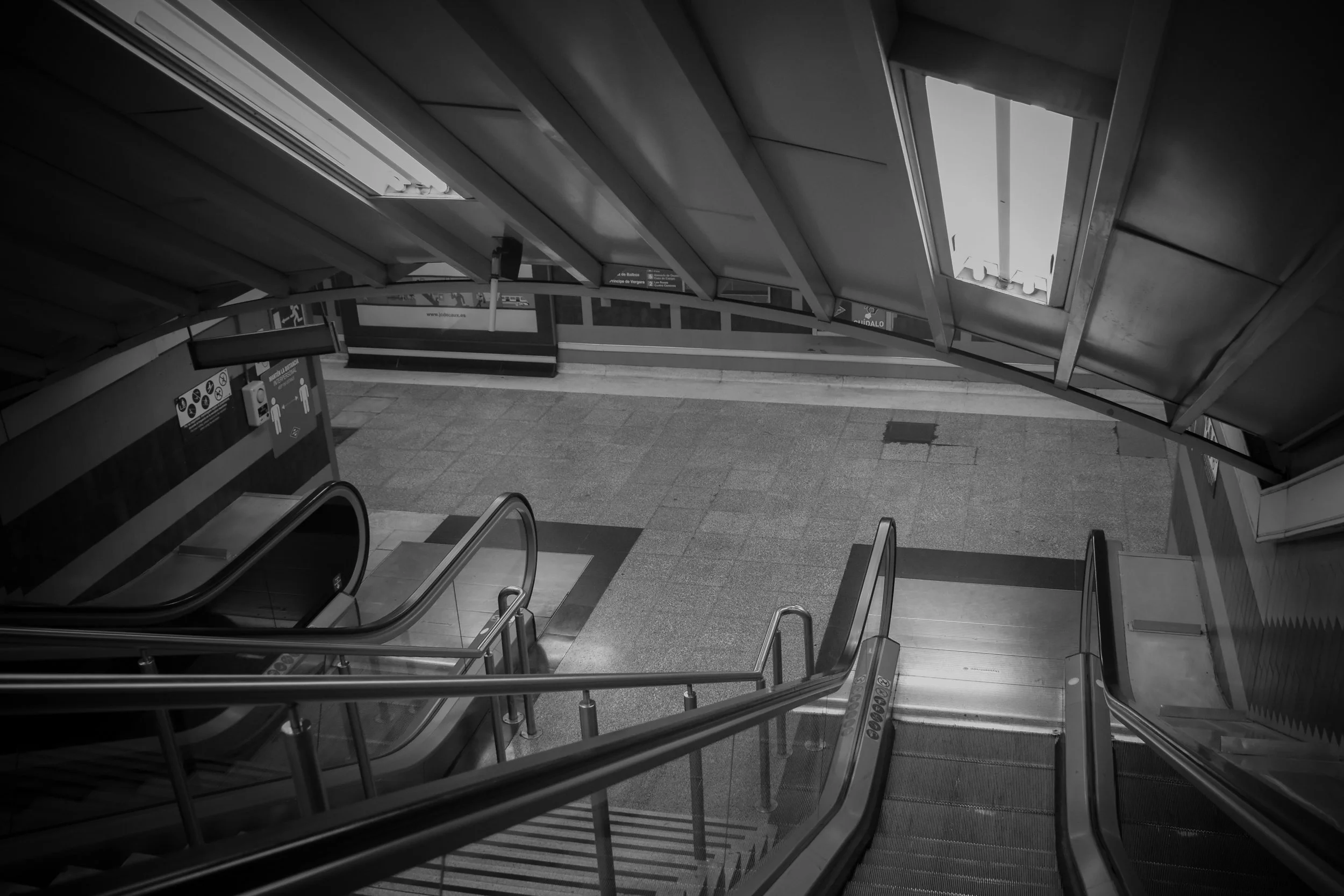 Black and white photo of an indoor staircase and escalator at a subway or train station with directional signs.