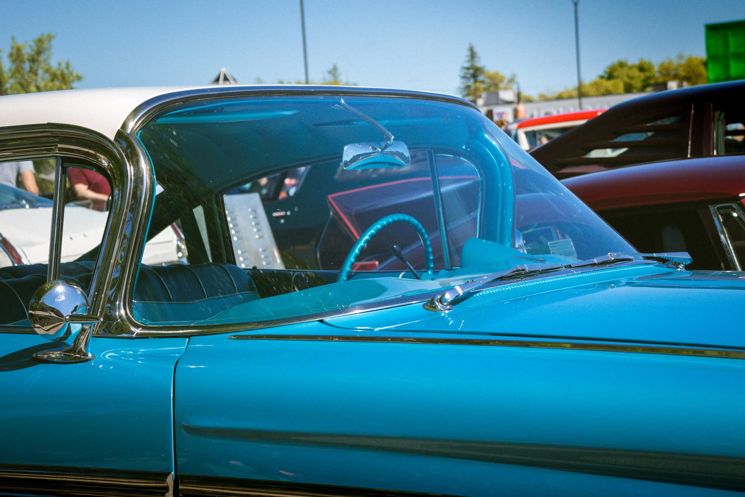 Close-up of a vintage blue car with a bubble-shaped windshield at a car show, other classic cars and people in the background.