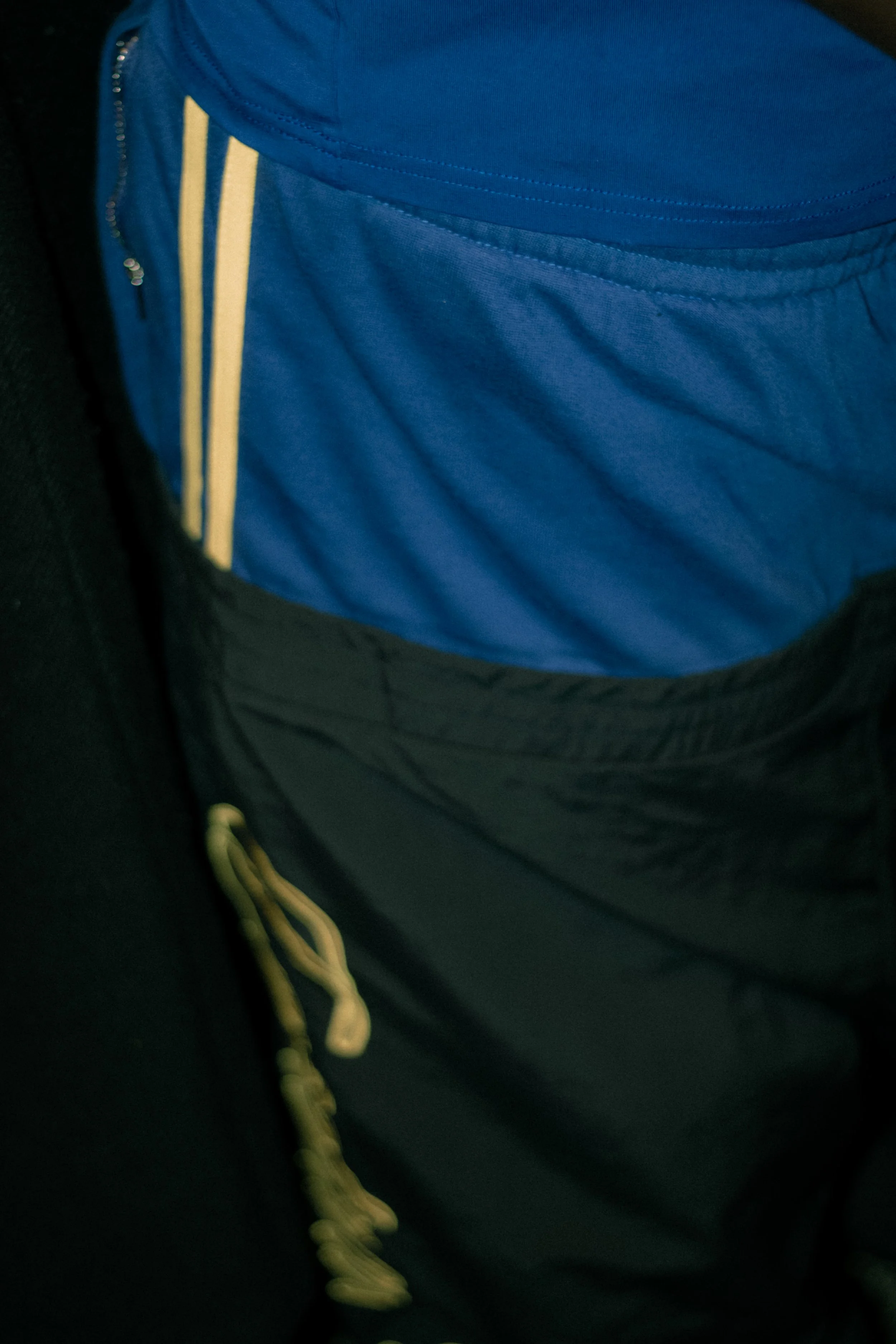 Close-up of a person wearing a blue Nike sports jacket with yellow stripes and a black zipper, dark pants, and yellow drawstrings.