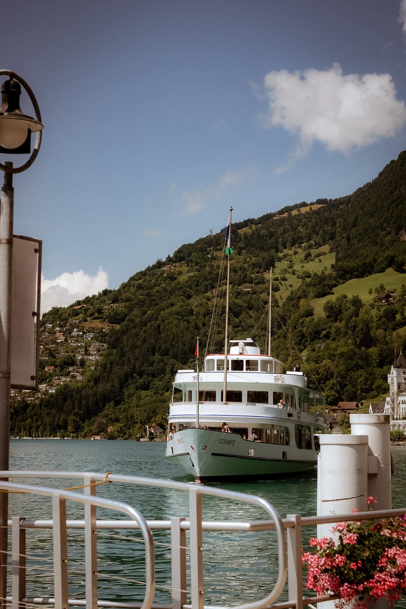A white yacht named Schwz cruising in a lake with mountains and green hills in the background, in a sunny day.