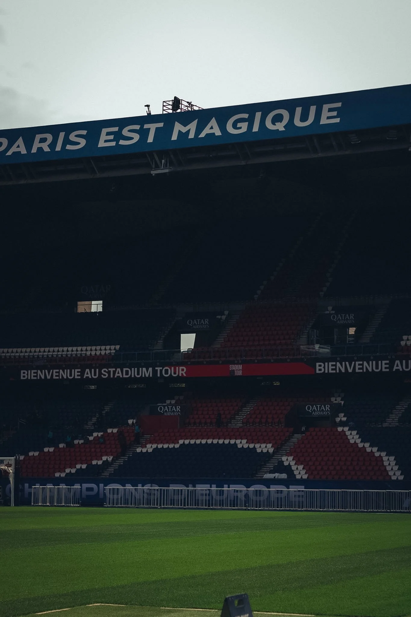 Empty football stadium with a green field, red seats, and large banners displaying French text and Qatar Airways logos.