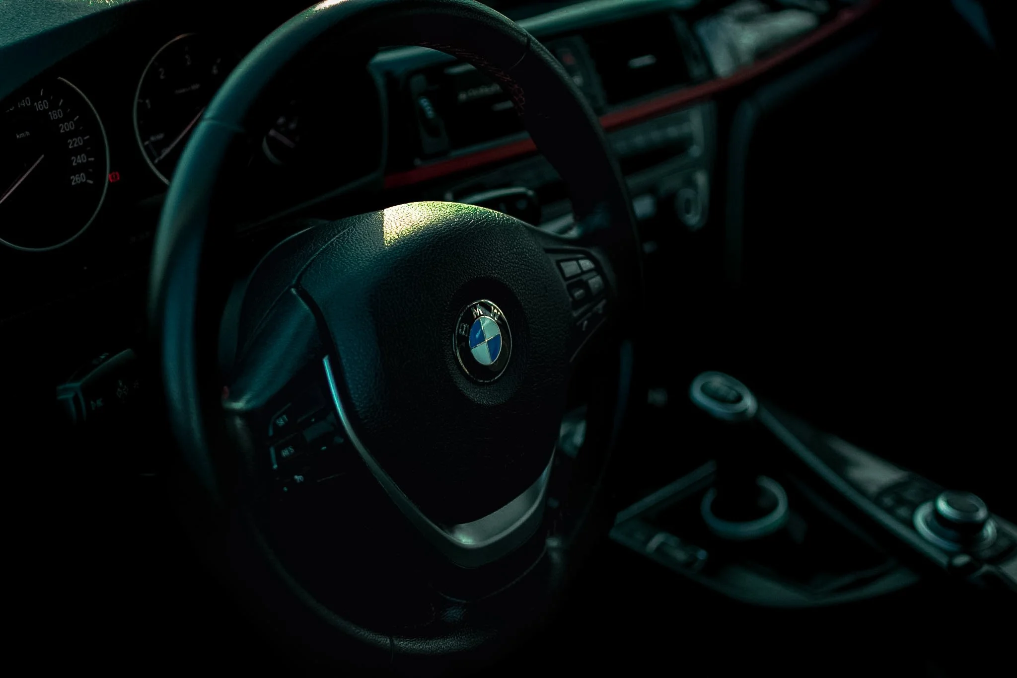 Close-up of a BMW steering wheel inside a car, with the dashboard and instrument cluster visible in the background.