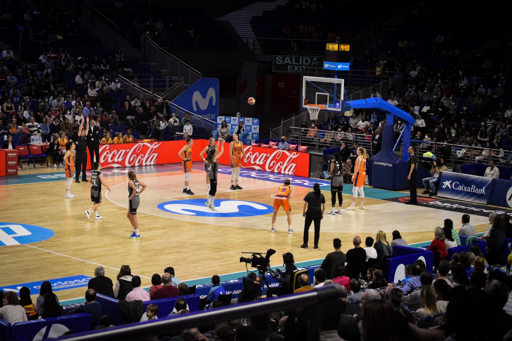 A basketball game in progress on an indoor court with players, referees, and spectators.